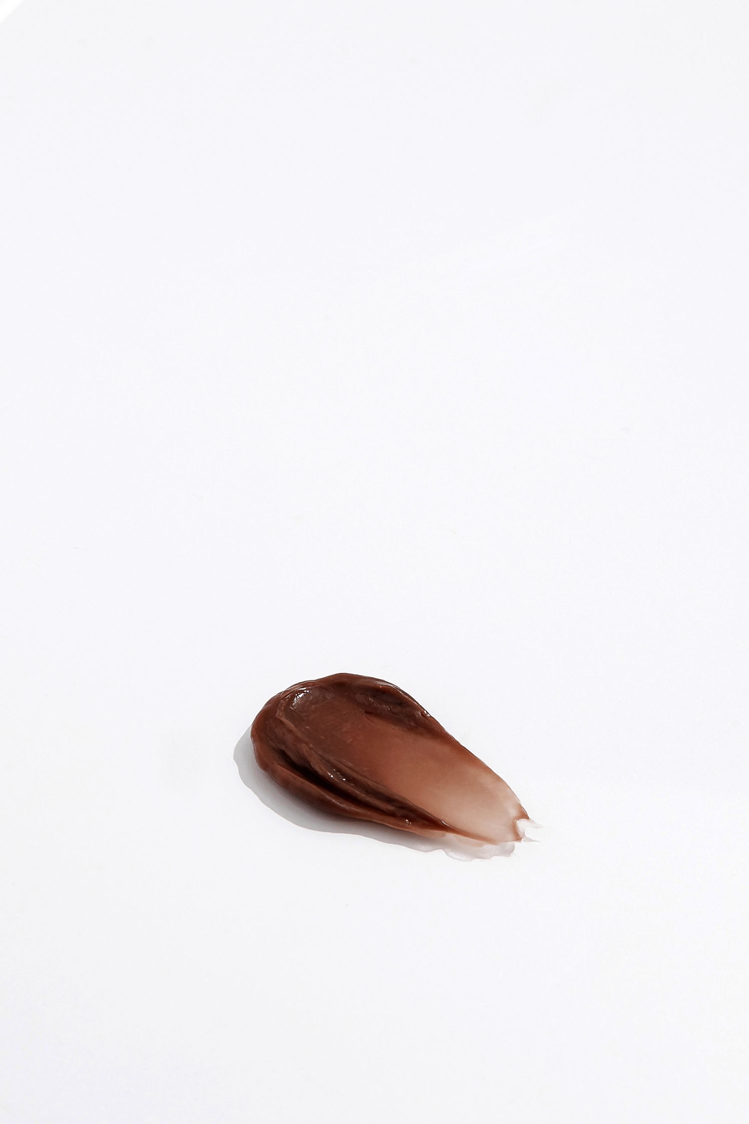 Single drop of bronze liquid makeup product on white background.