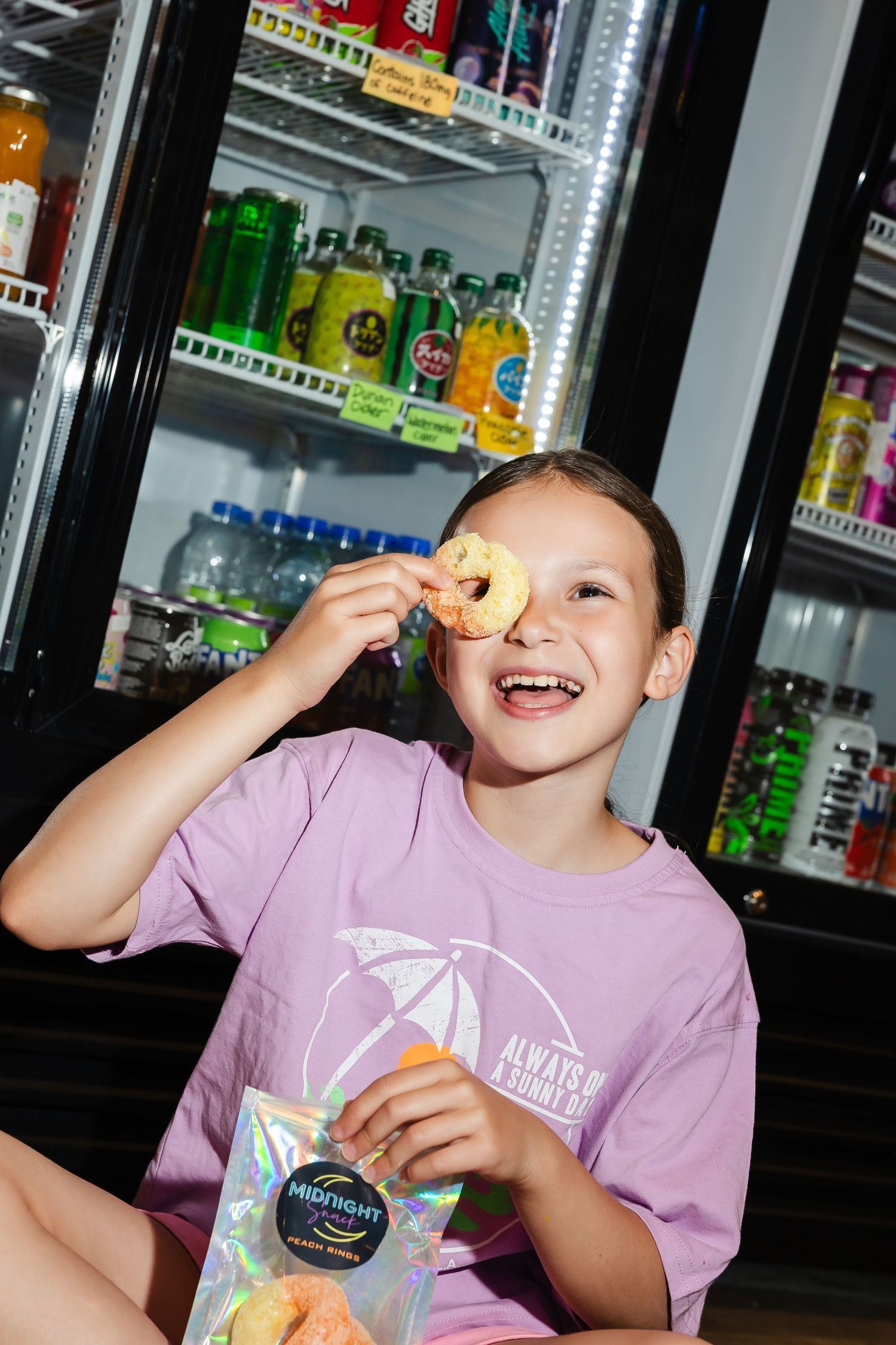 Child in purple shirt enjoying snacks near beverage coolers.