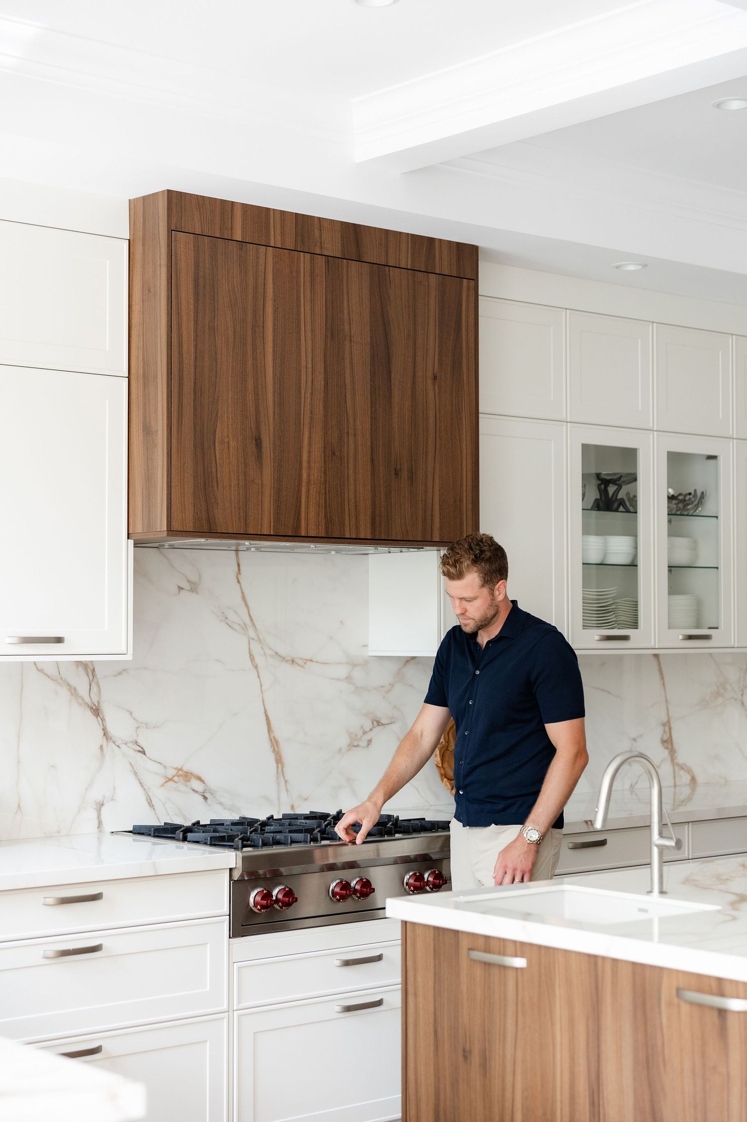 Man examines modern kitchen features with white cabinets and wood accents.