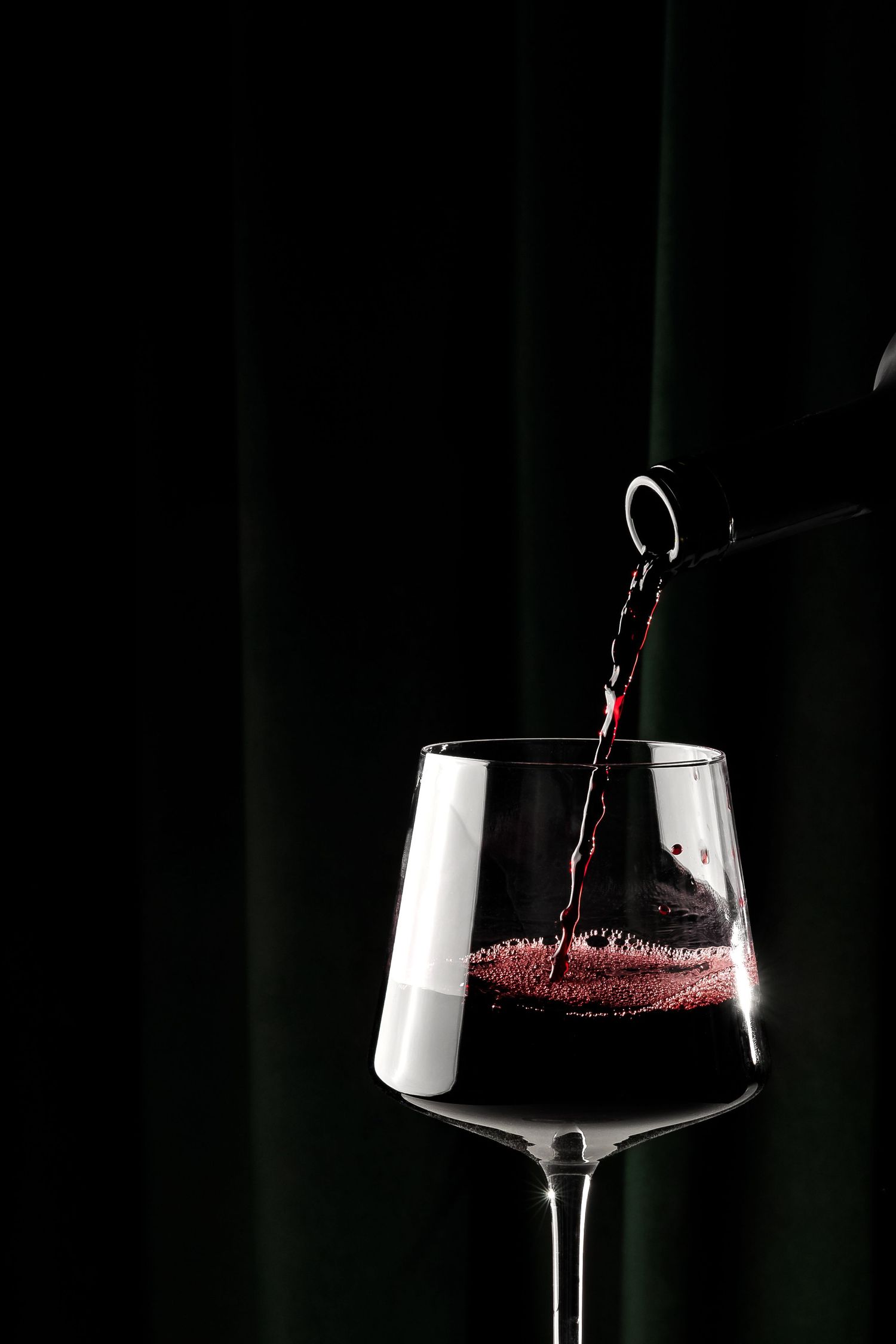 Deep red wine splashing as it's poured into a modern wine glass.