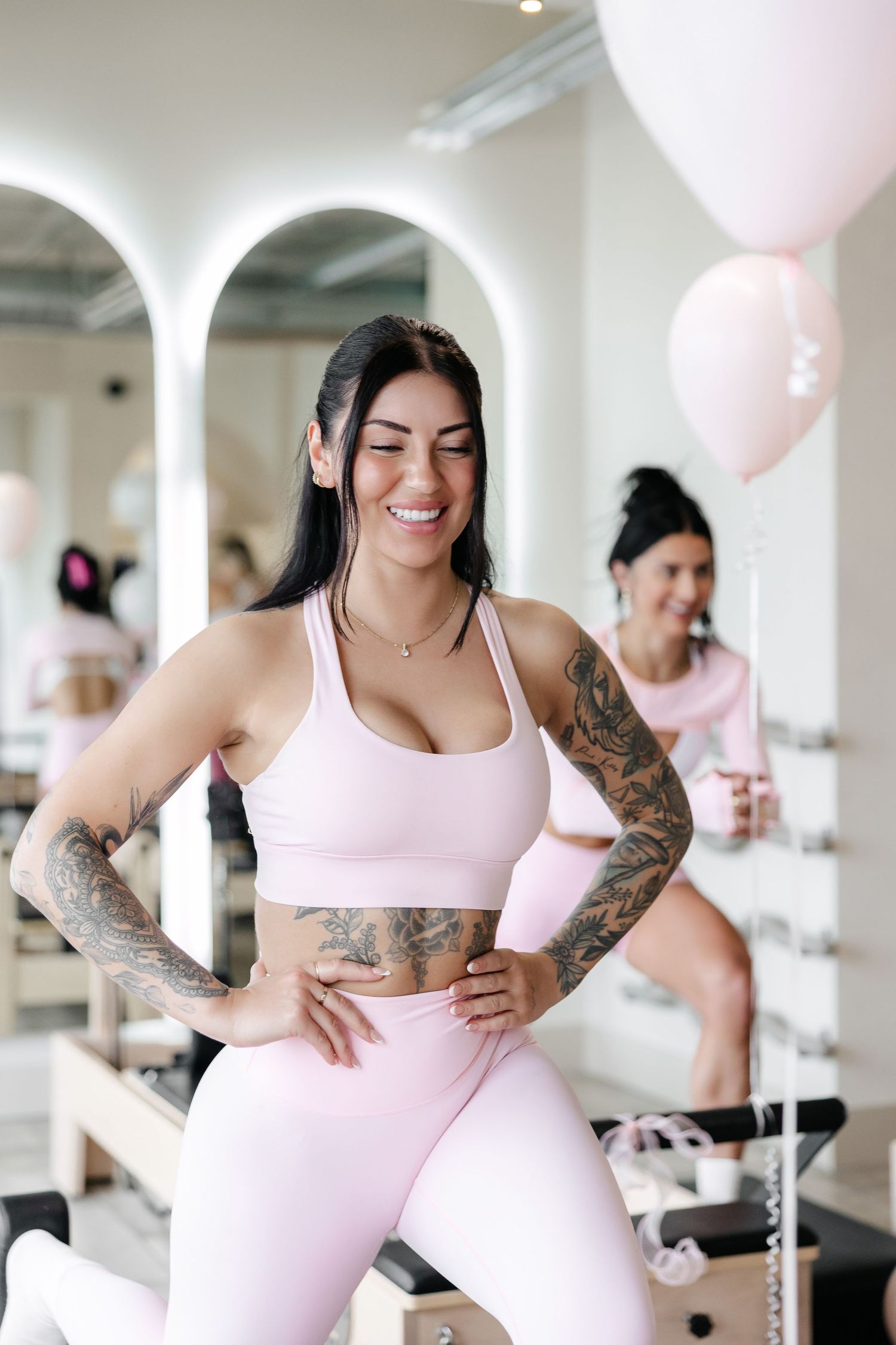 Person in pink workout gear demonstrating fitness poses in a bright studio with arched windows.