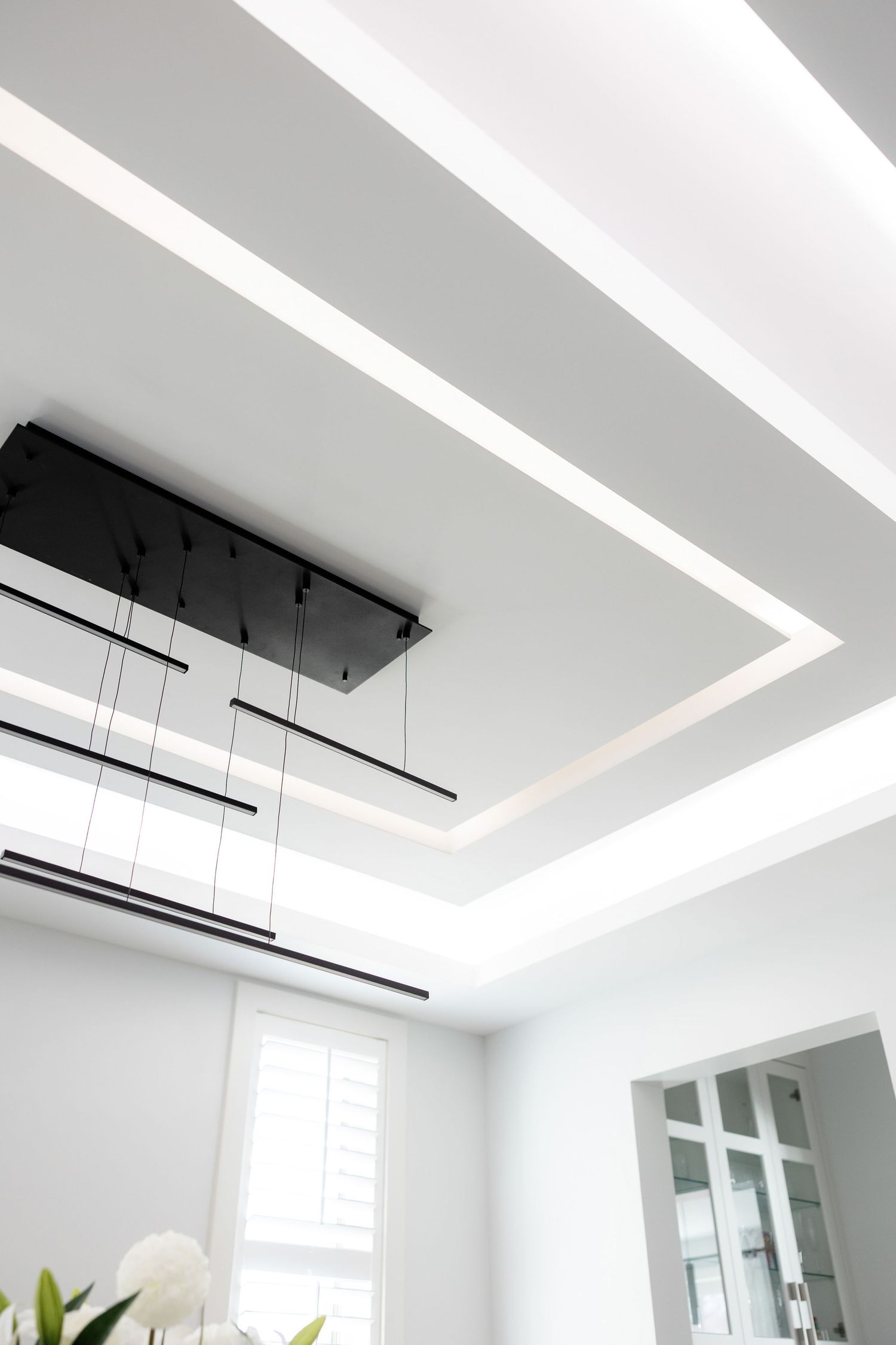 Modern white ceiling with recessed lighting and a sleek black pendant light fixture creating geometric patterns.