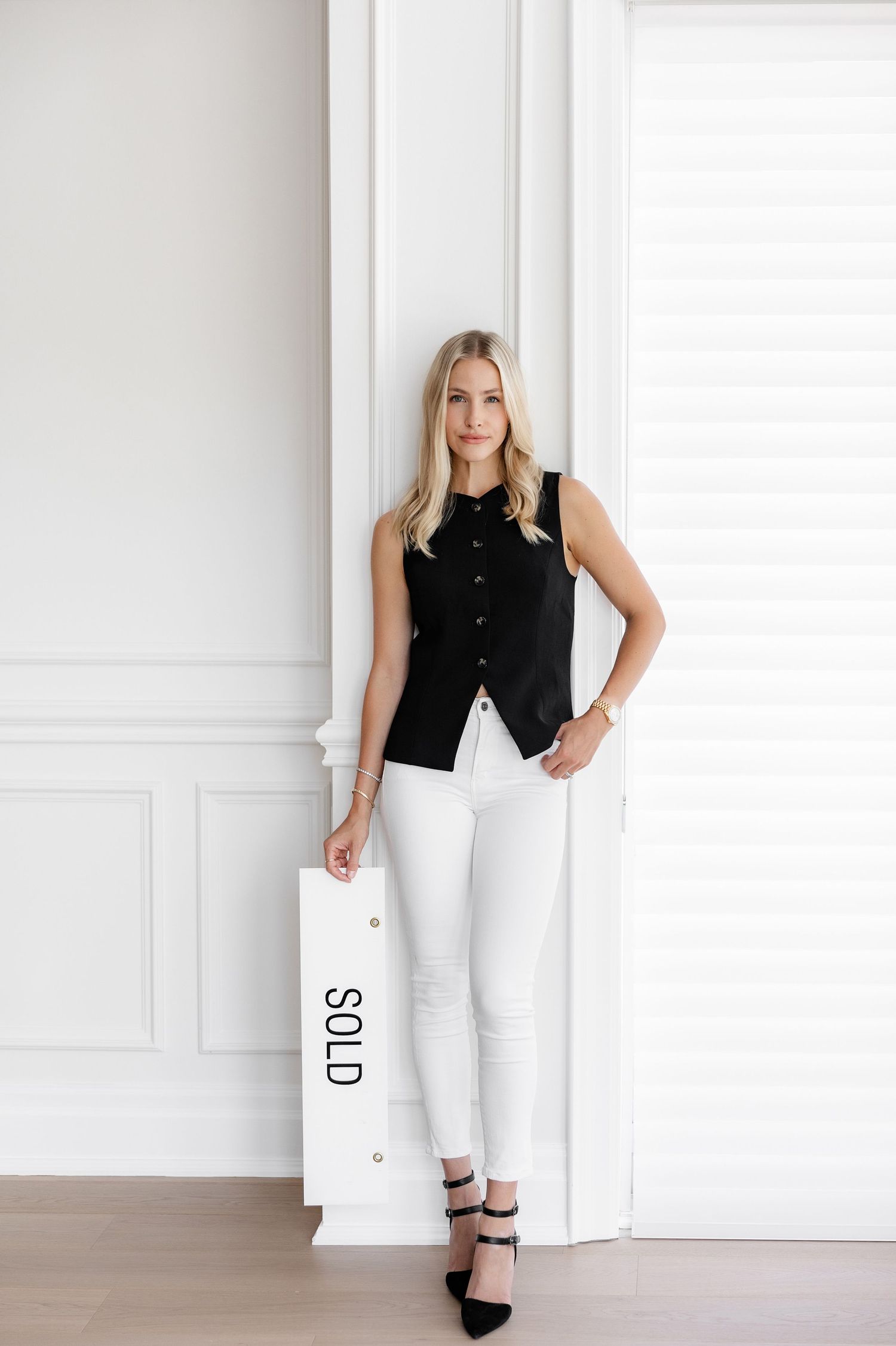 Stylish outfit featuring a black sleeveless top paired with crisp white pants and black heels against a white wall.