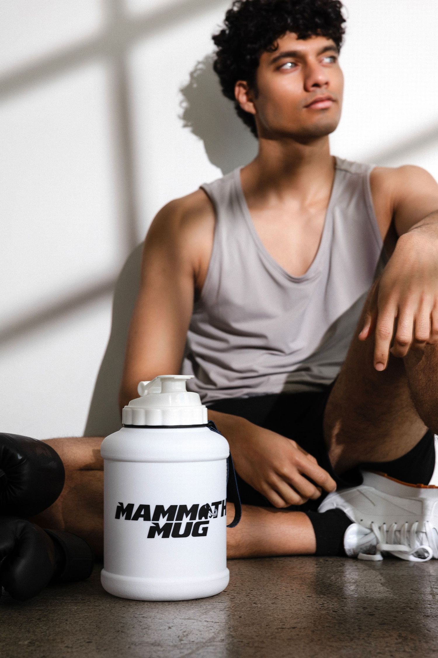 Model in gray tank top poses with white branded containers in dramatic window lighting.