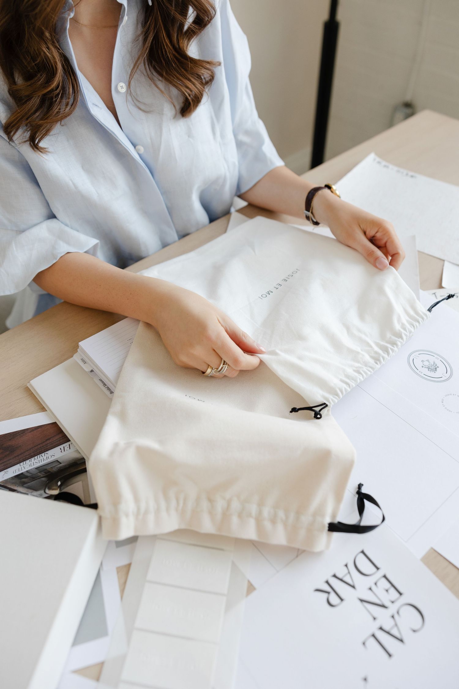 Hands arranging white fabric pouch and documents on wooden desk surface.