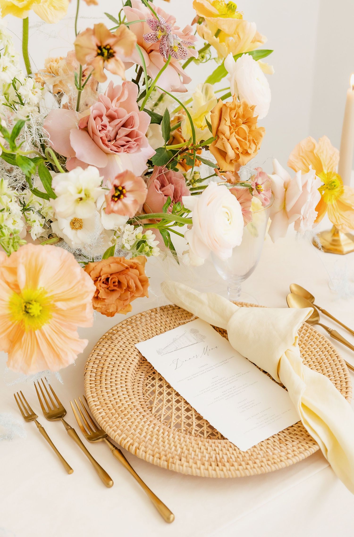 Elegant place setting with woven charger plate, white dinnerware and gold flatware adorned with spring flowers.