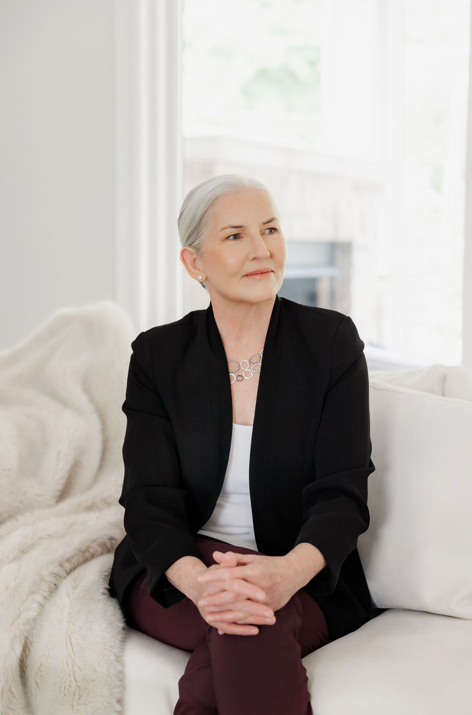 Professional in black blazer sitting on white couch in bright modern interior.