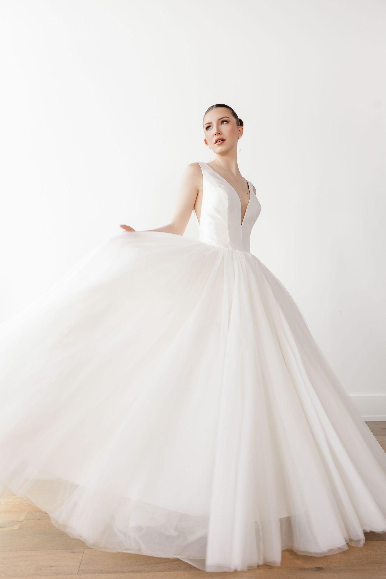 Dramatic ball gown wedding dress with full tulle skirt in motion against wooden floor.