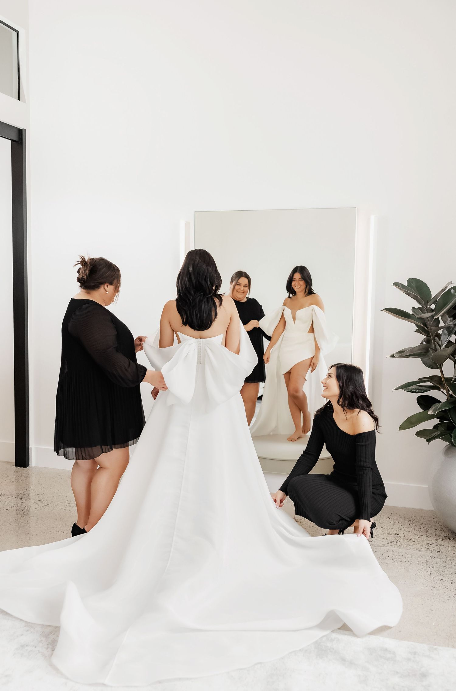 Behind-the-scenes of bridal fitting with assistants helping arrange a flowing white wedding gown in a modern studio.