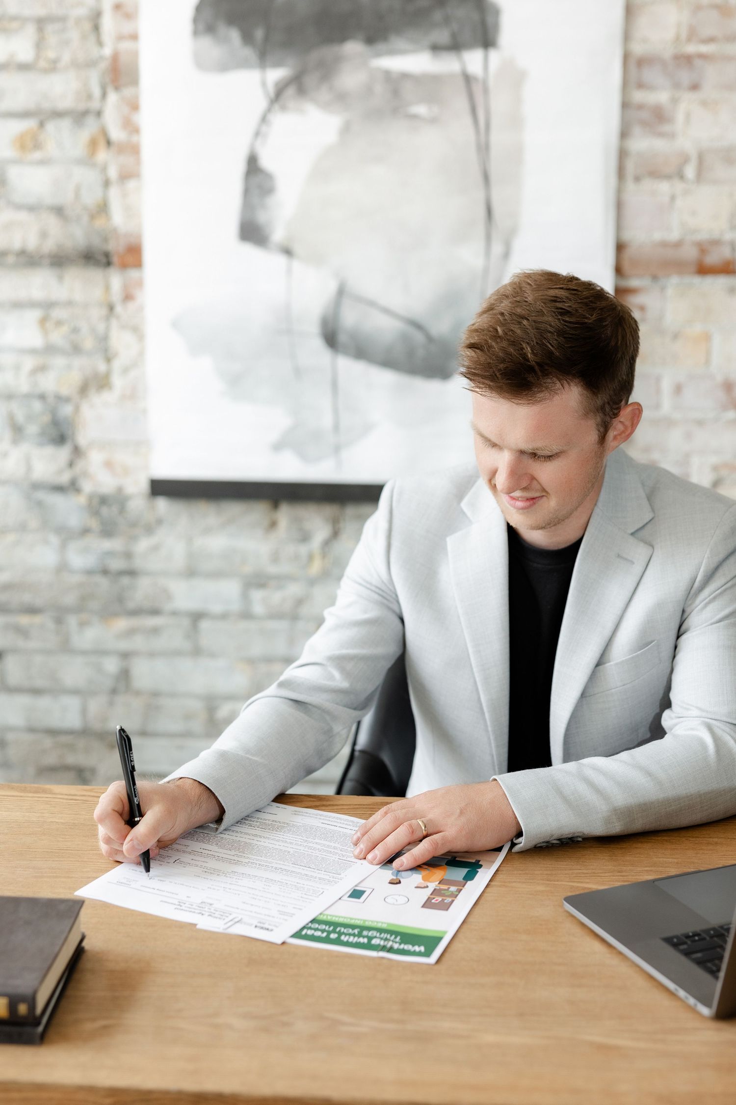 Person in white blazer works at desk with laptop and documents in bright office setting.