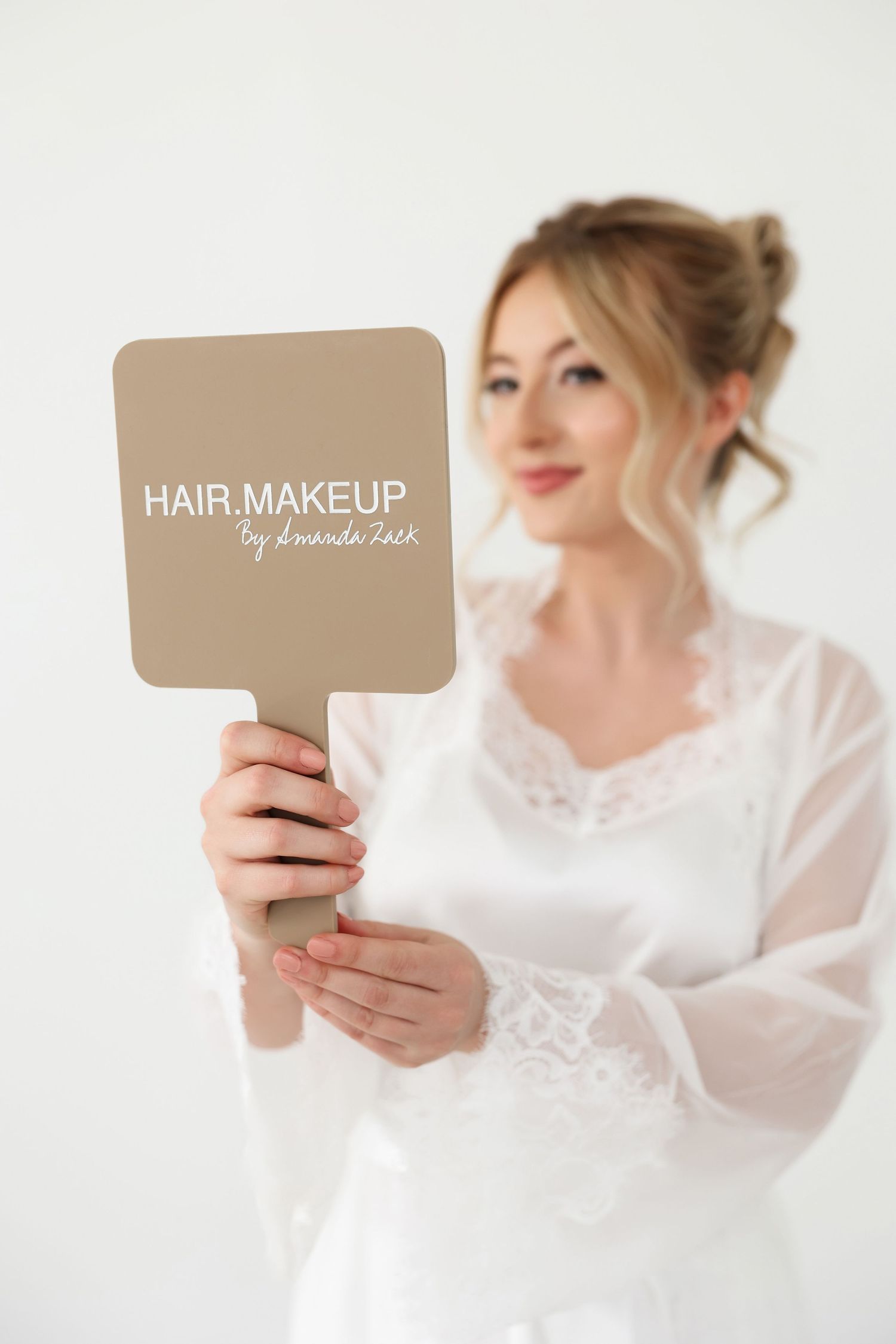 Person in white lace robe holding hair and makeup service sign during bridal preparation.