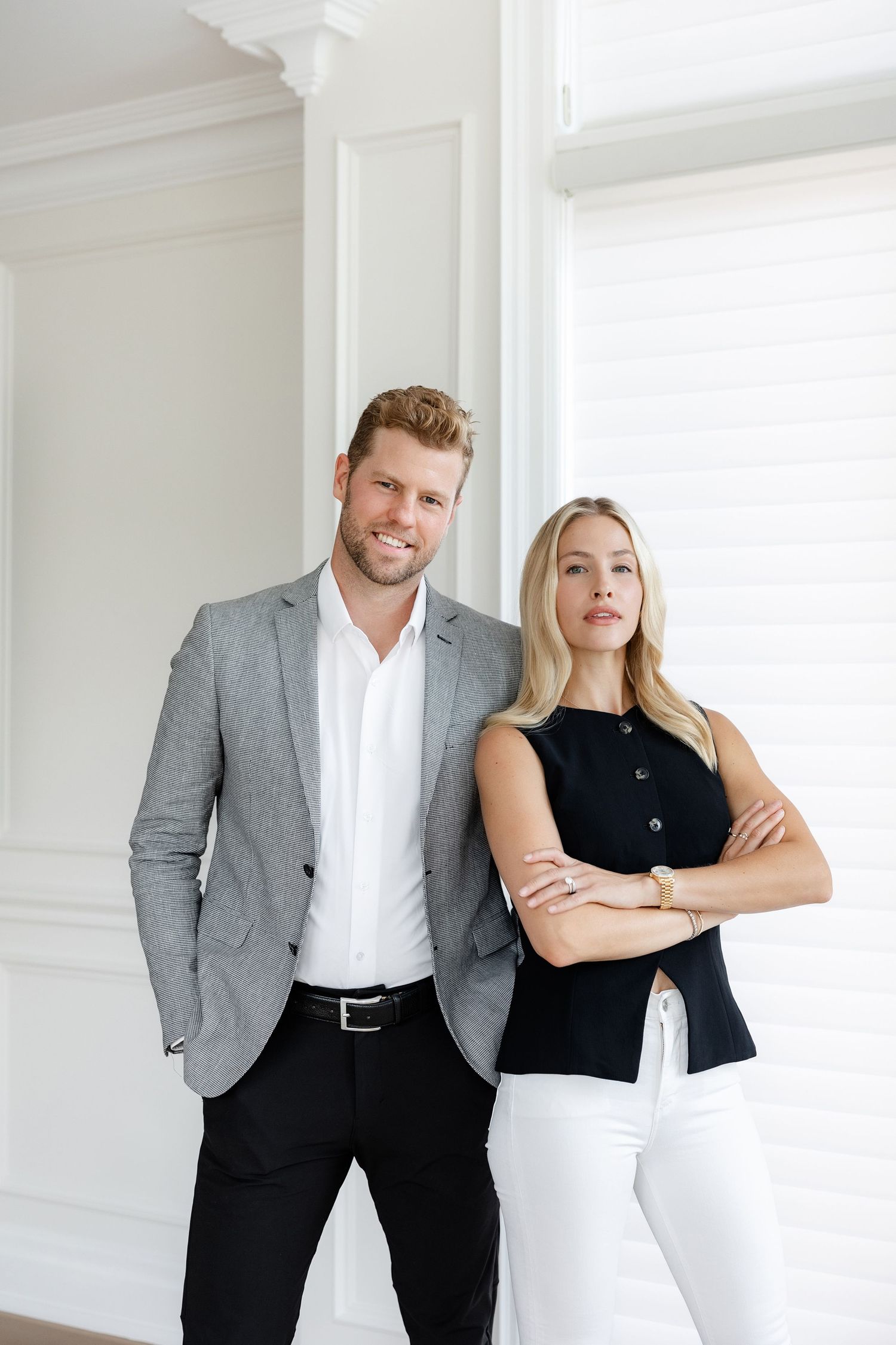 Business professionals in formal attire standing confidently against white wall.