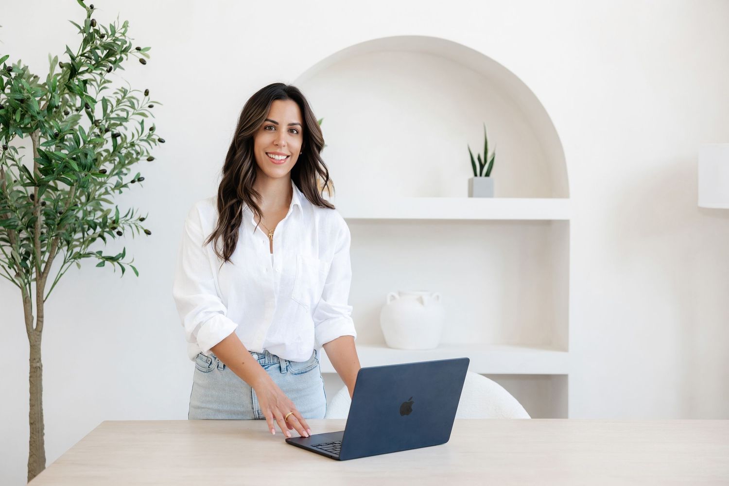 Person working on laptop in minimalist white room with plants and built-in shelving.