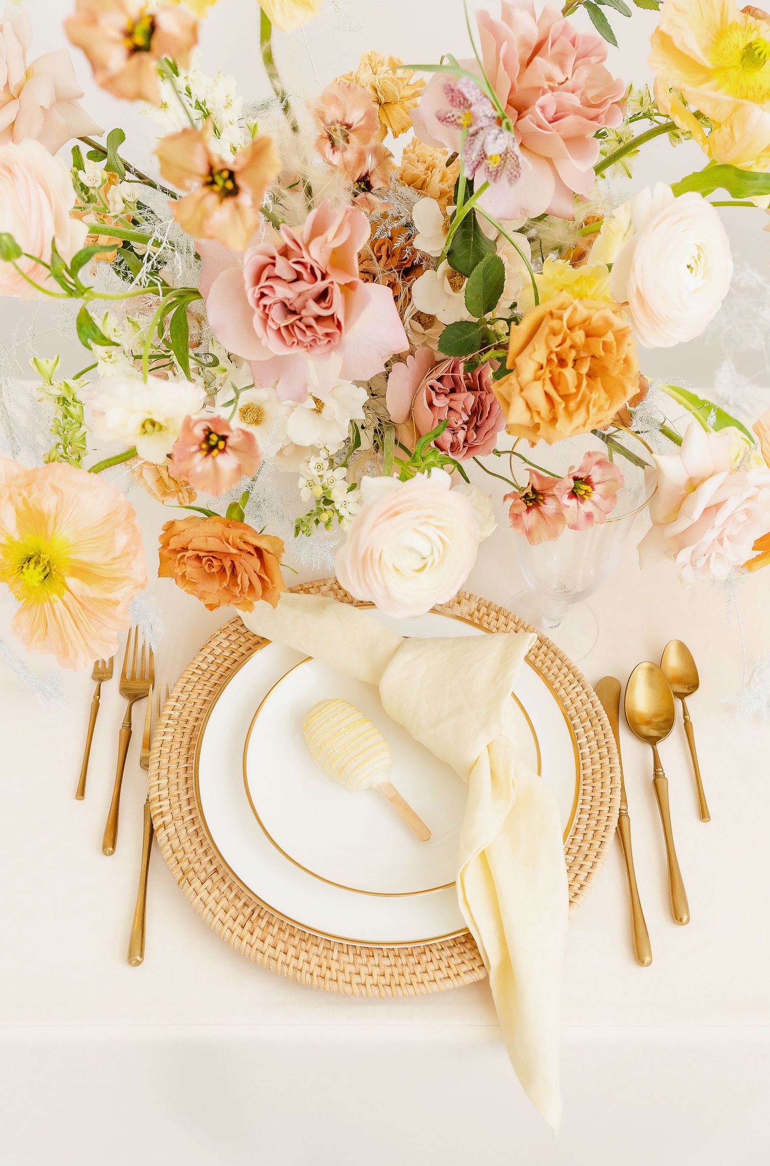 Romantic table setting with cream napkins, gold cutlery and pastel floral arrangements.