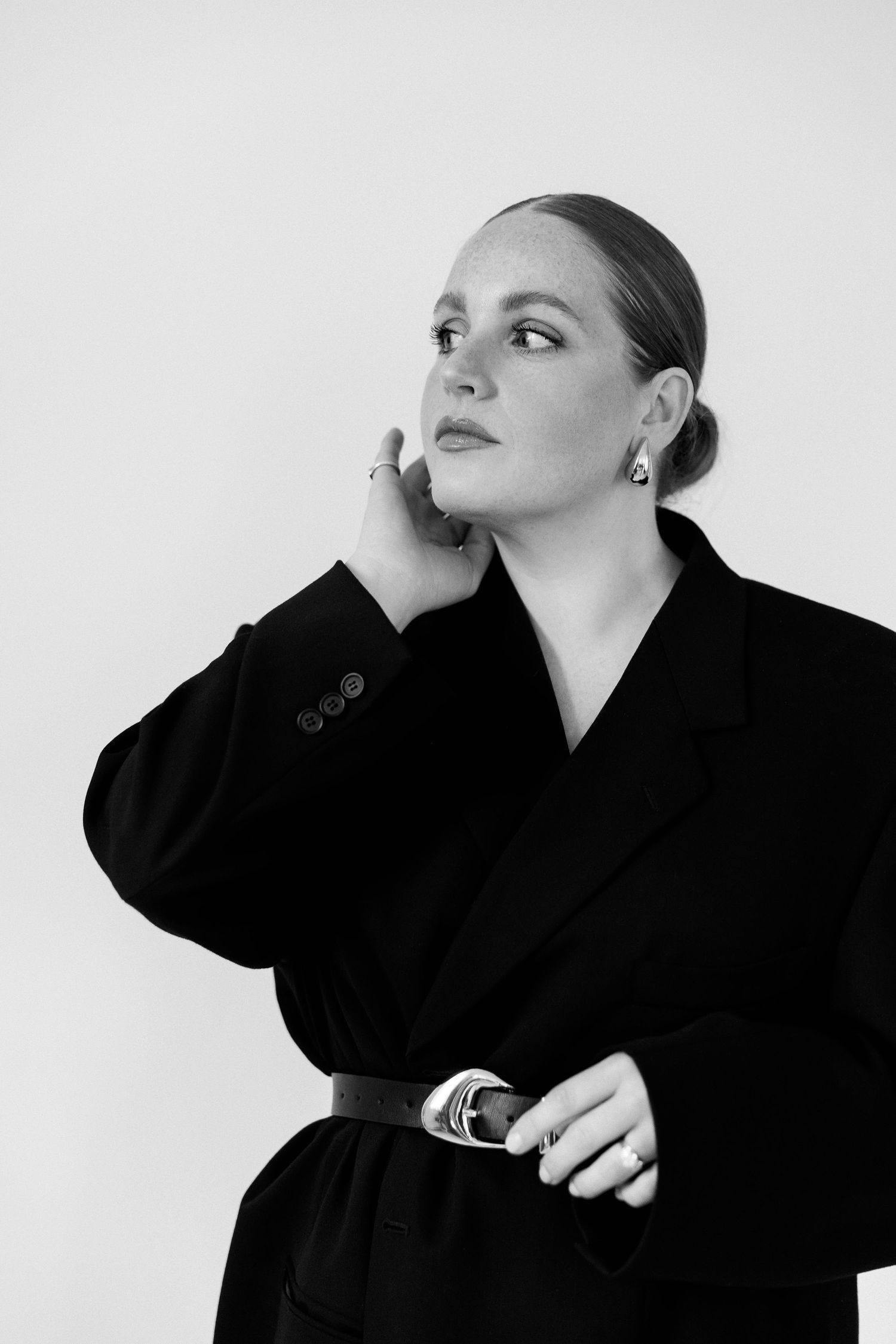 Stylish portrait in black blazer with belted waist against white background.