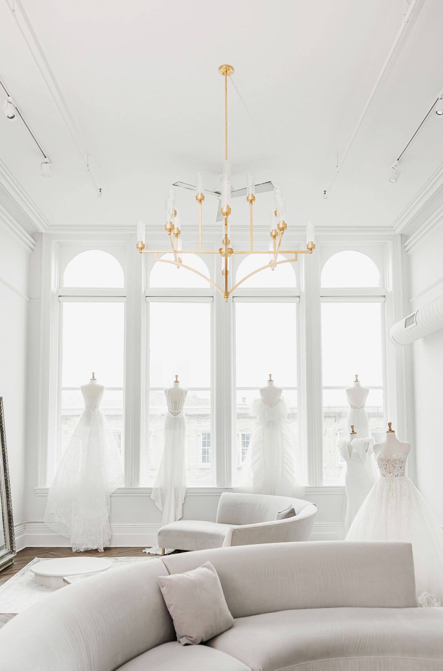 Bright white bridal boutique interior with curved sofa and elegant chandelier lighting.