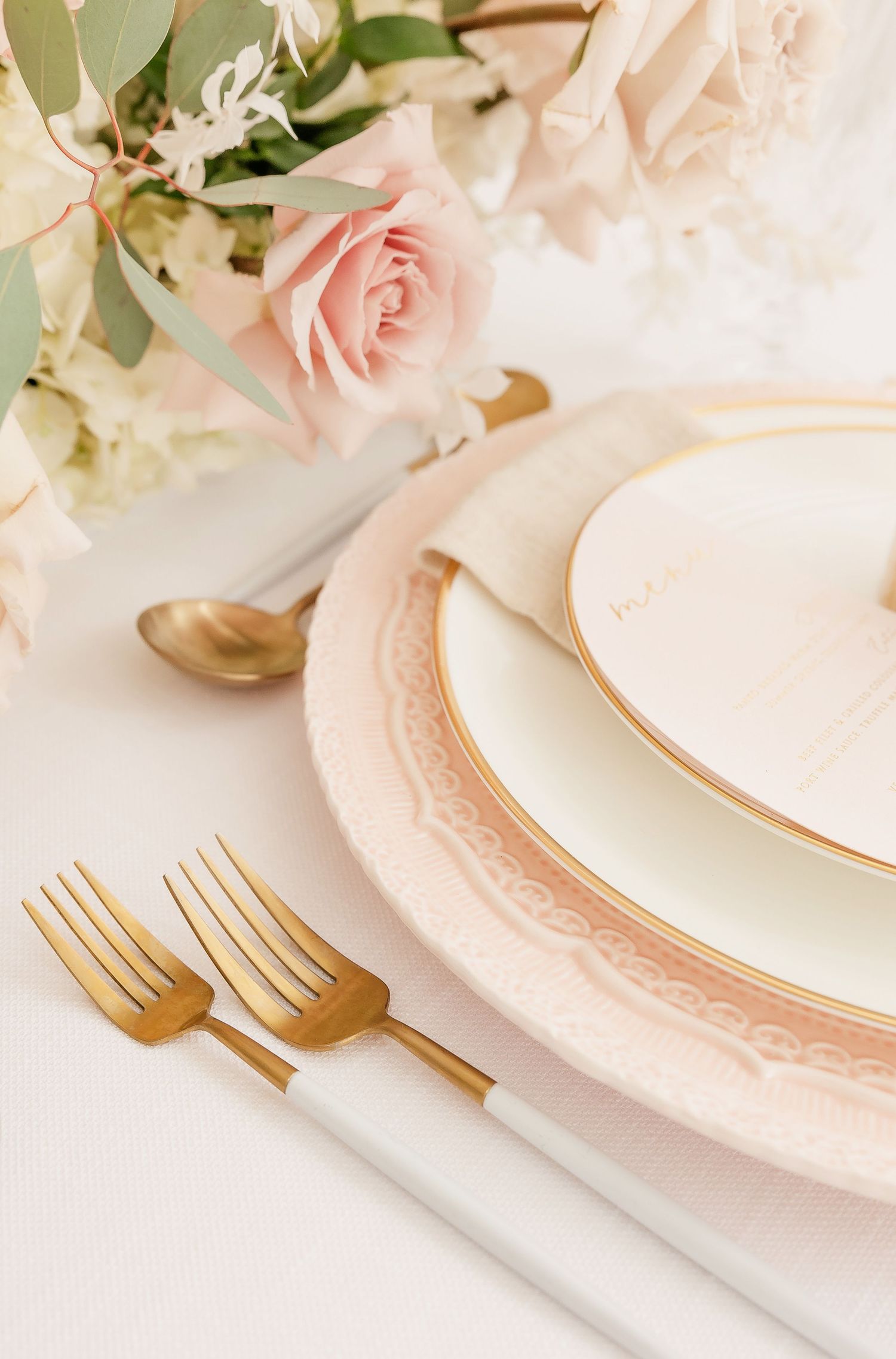 Wedding table setup with gold flatware and pink-rimmed plates.
