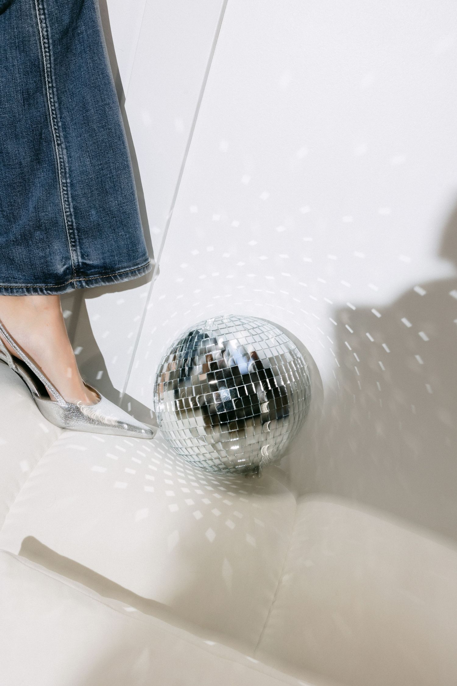 Disco ball creates sparkly reflections against white studio wall with silver heels visible.
