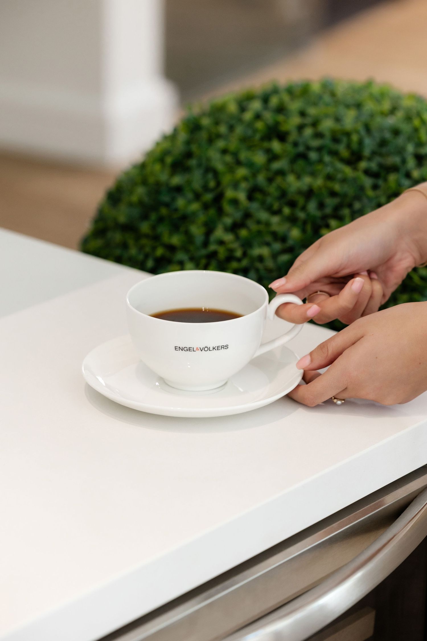 Hands placing white coffee cup and saucer on minimalist white surface.