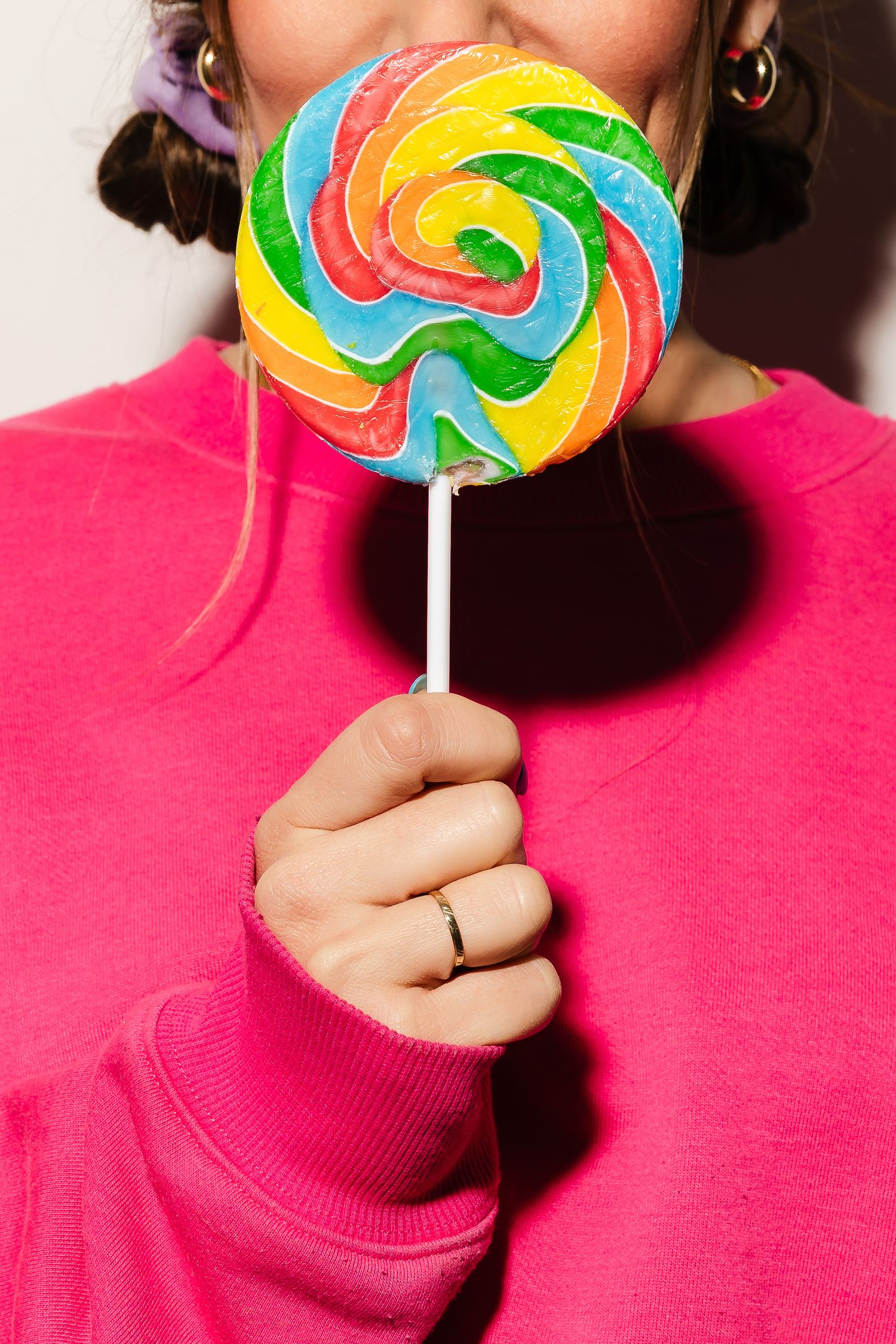 Colorful spiral lollipop held against bright pink background.