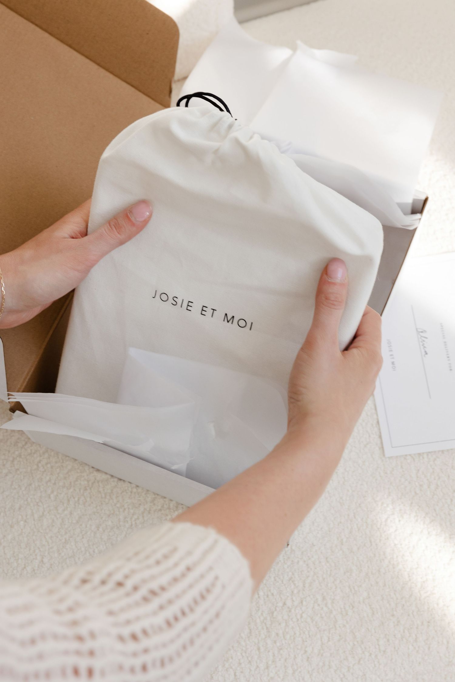 Hands holding white fabric bag with Josie et Moi branding in natural light.