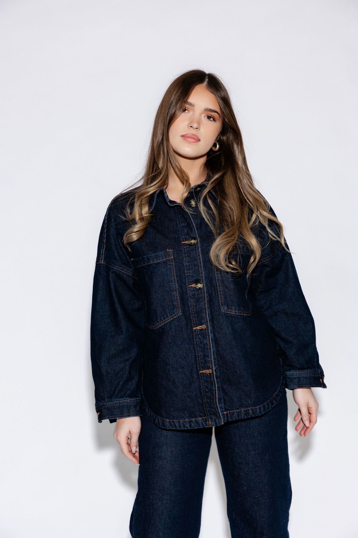 Model showcases dark denim jacket ensemble in studio photoshoot against white background.