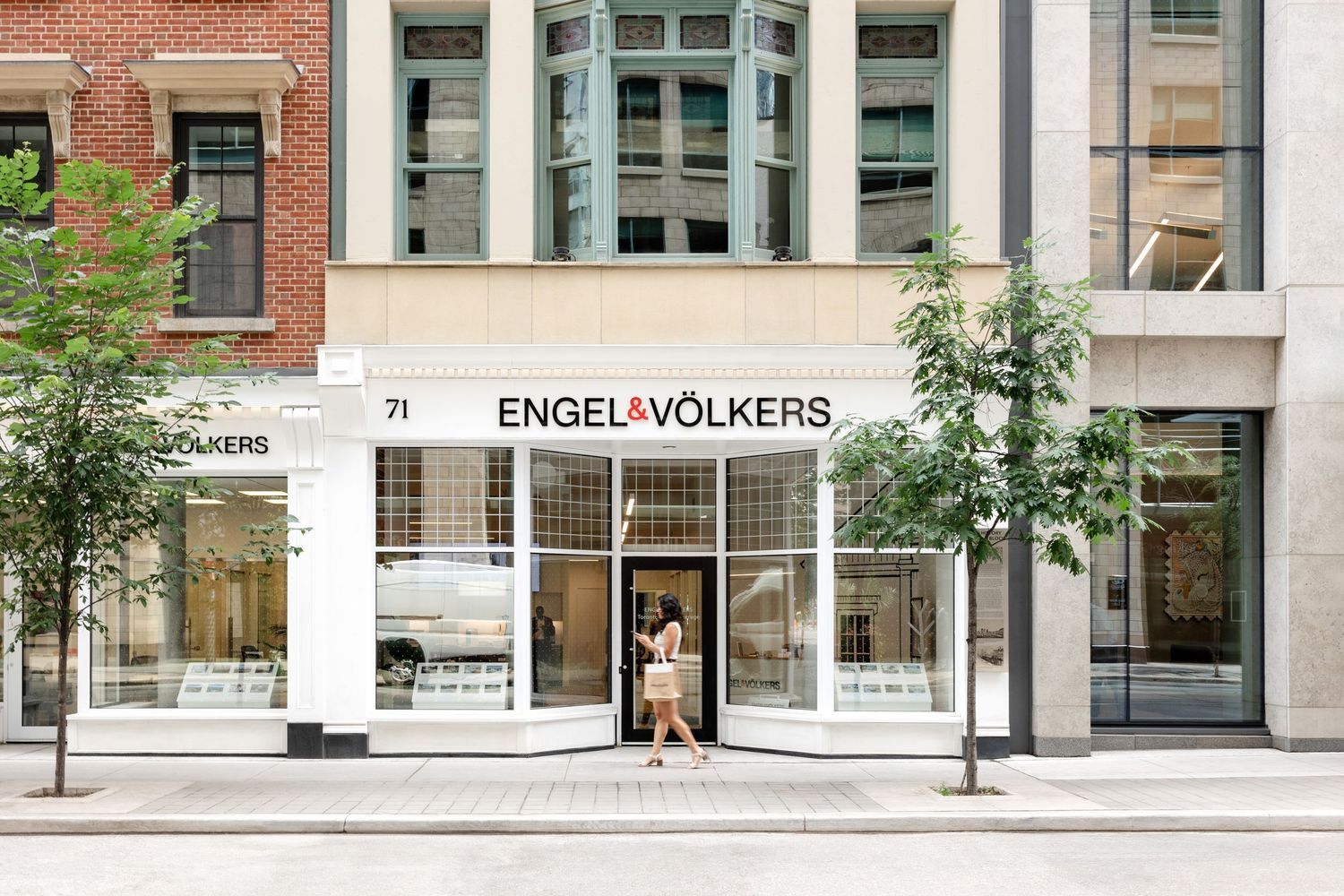 Street view of Engel & Volkers storefront in brick building with bay windows.