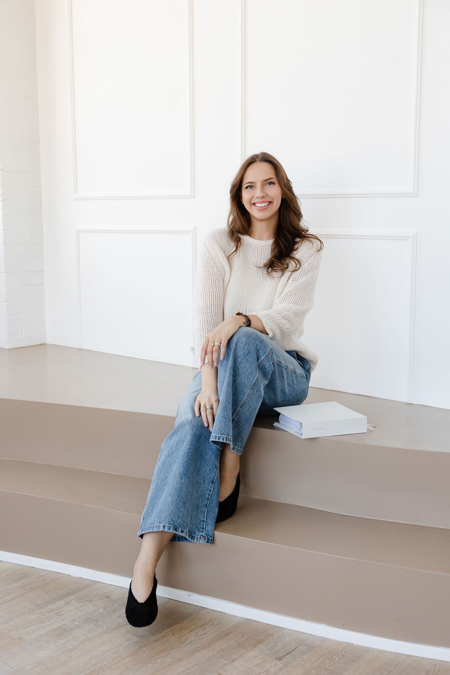 Lifestyle portrait on steps wearing cream sweater and relaxed denim.
