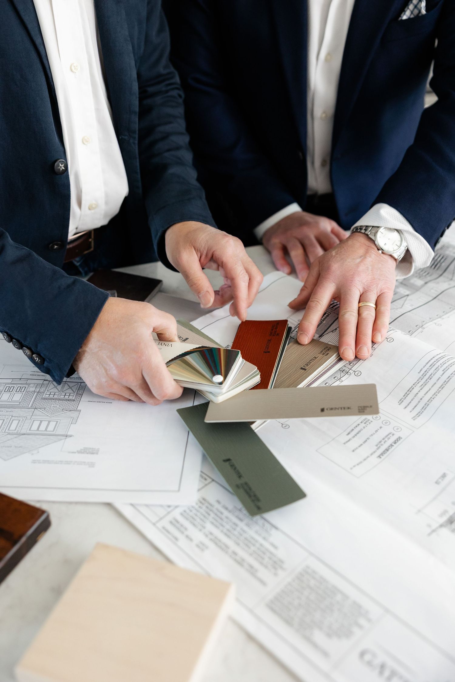Business professionals reviewing documents and handling paperwork on a desk with various materials spread out.