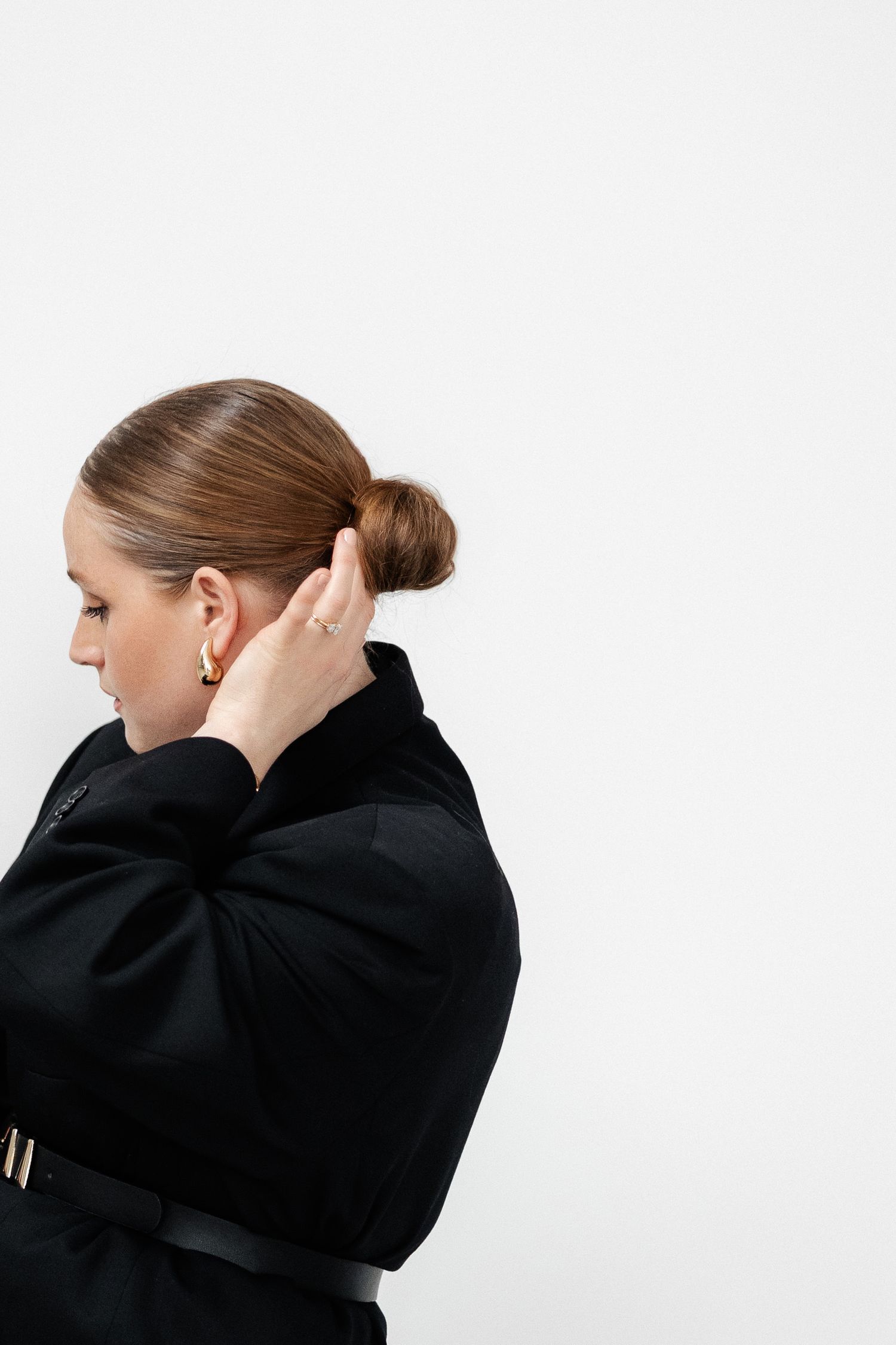 Person in black sweater adjusts hair in minimalist studio portraits.