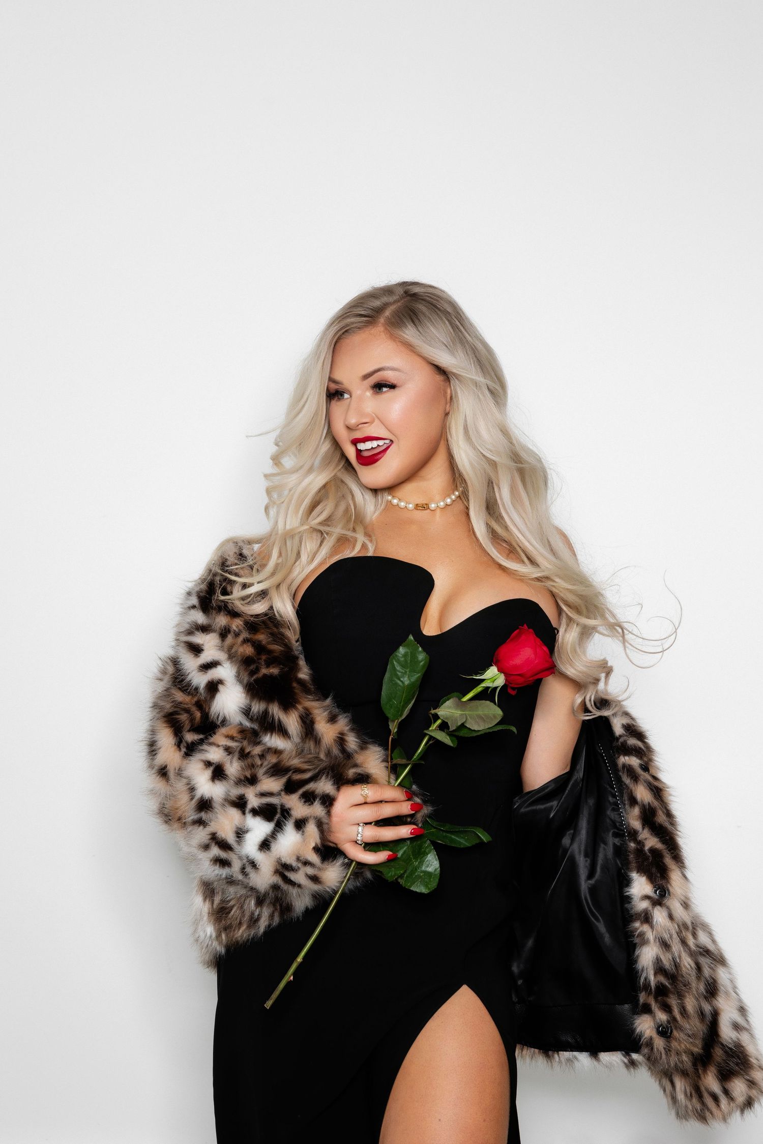 Glamorous scene with leopard print fur coat and red rose against white background.