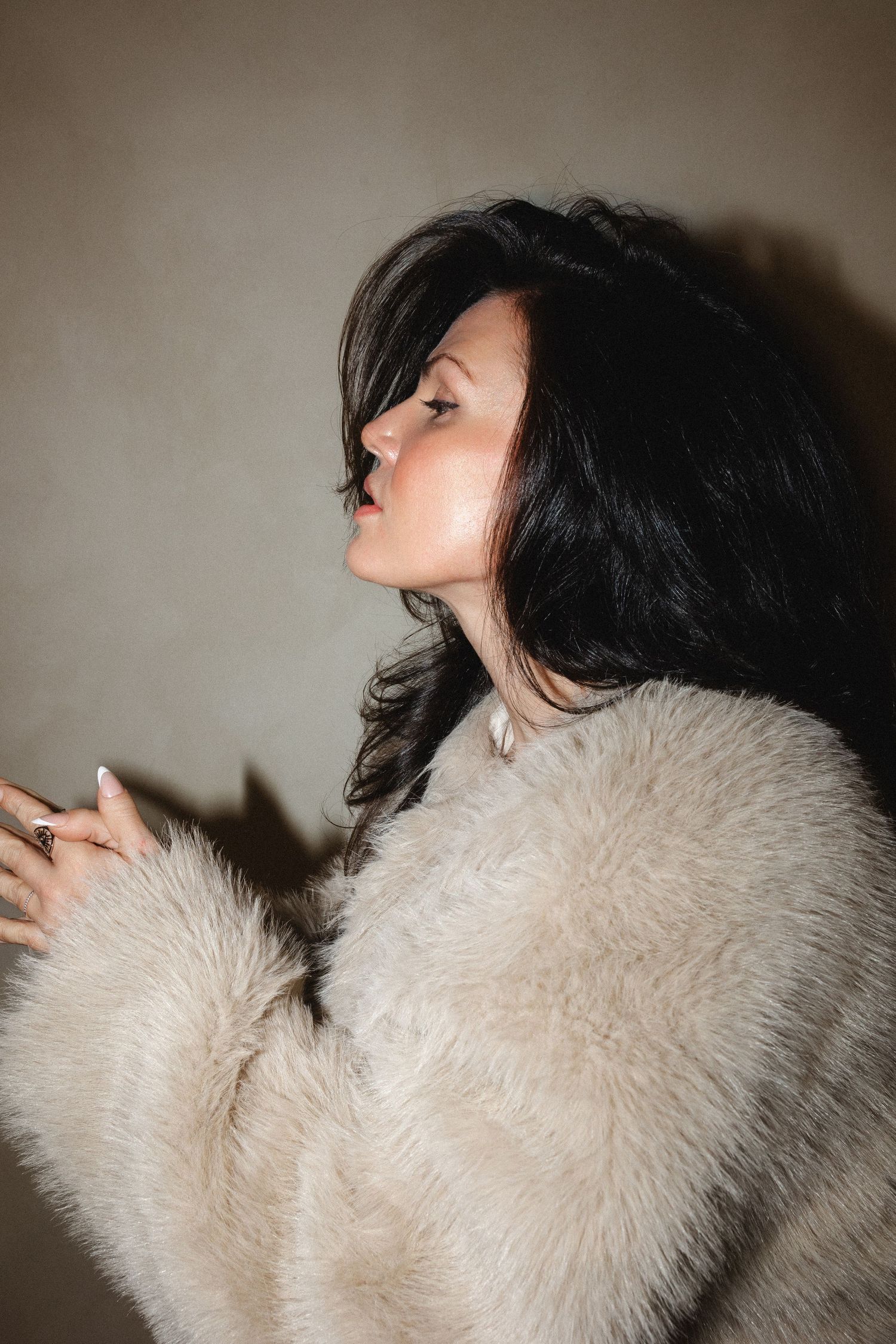 Side profile shot of model wearing plush beige coat in dramatic lighting.