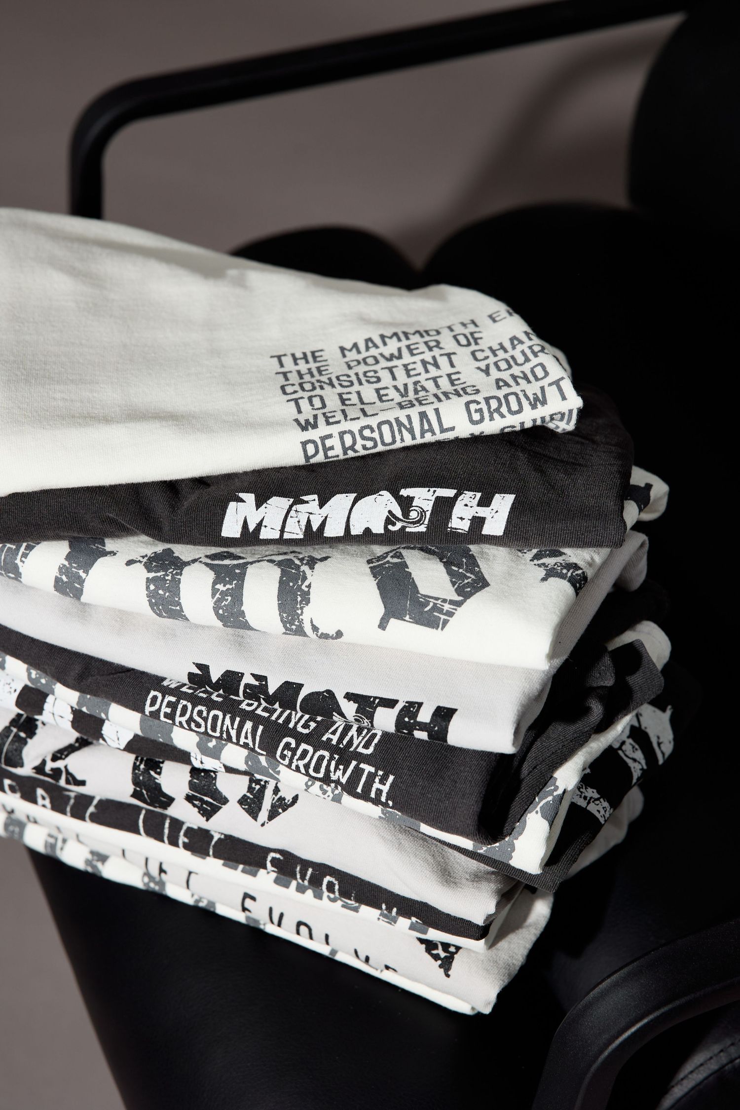 Folded white t-shirts with black gothic text prints displayed in monochrome.