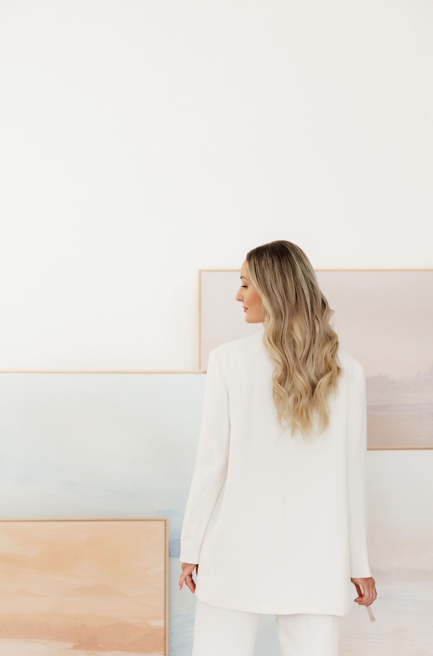 Person arranging minimal artwork collection on white wall.