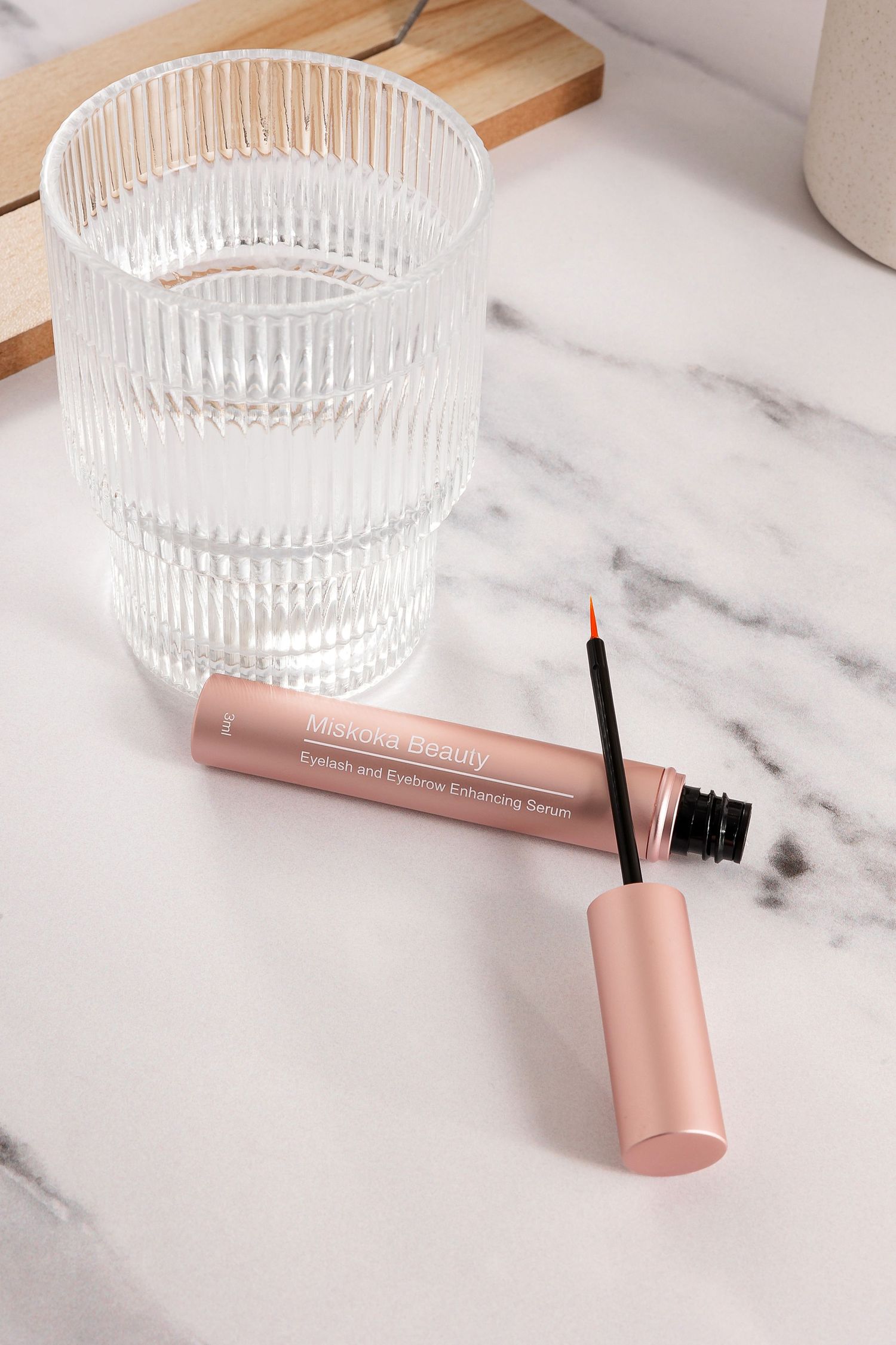 Rose gold mascara tube next to clear glass container on marble surface.