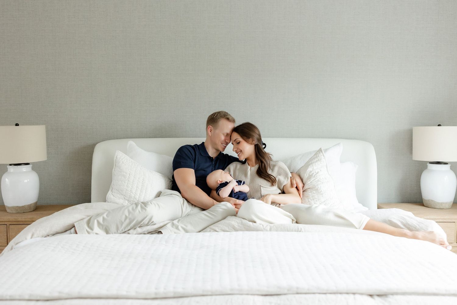 Family cuddle time captured in a serene white bedroom with natural lighting.