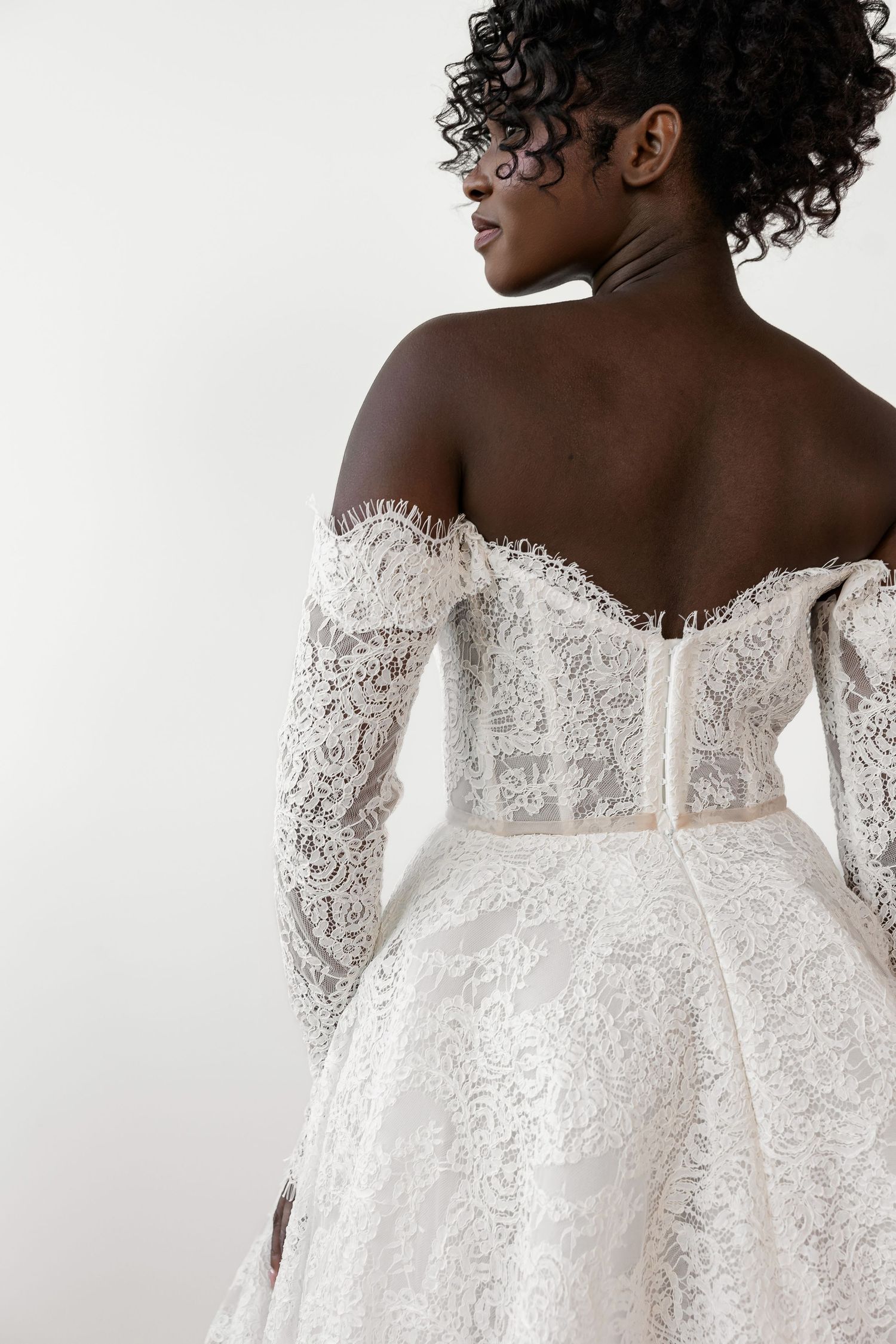 Off-shoulder lace wedding gown with sheer long sleeves shown from back view.
