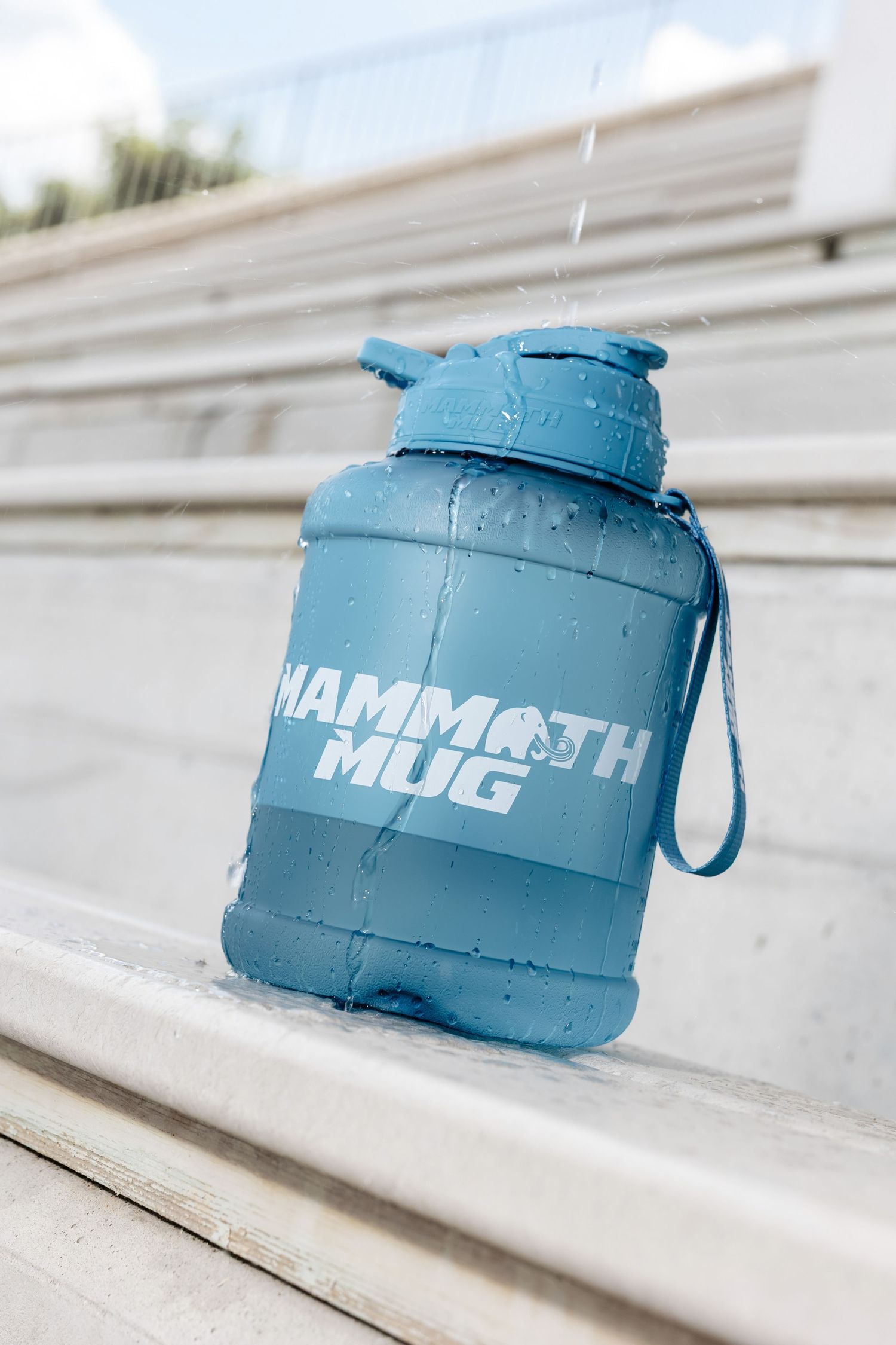 Blue mammoth water bottle sitting on white concrete stadium bleachers.