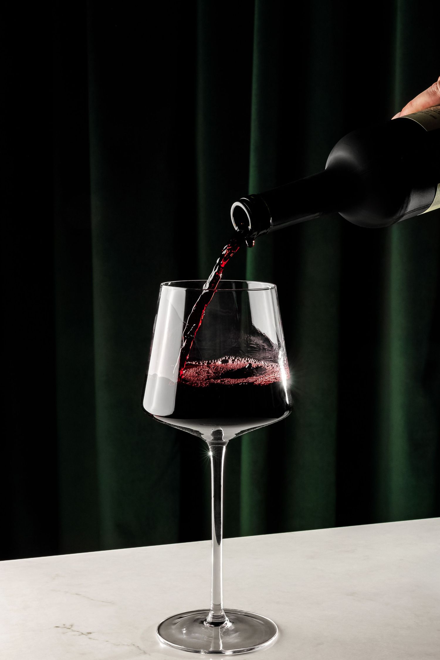 Red wine being poured into an elegant stemmed glass.