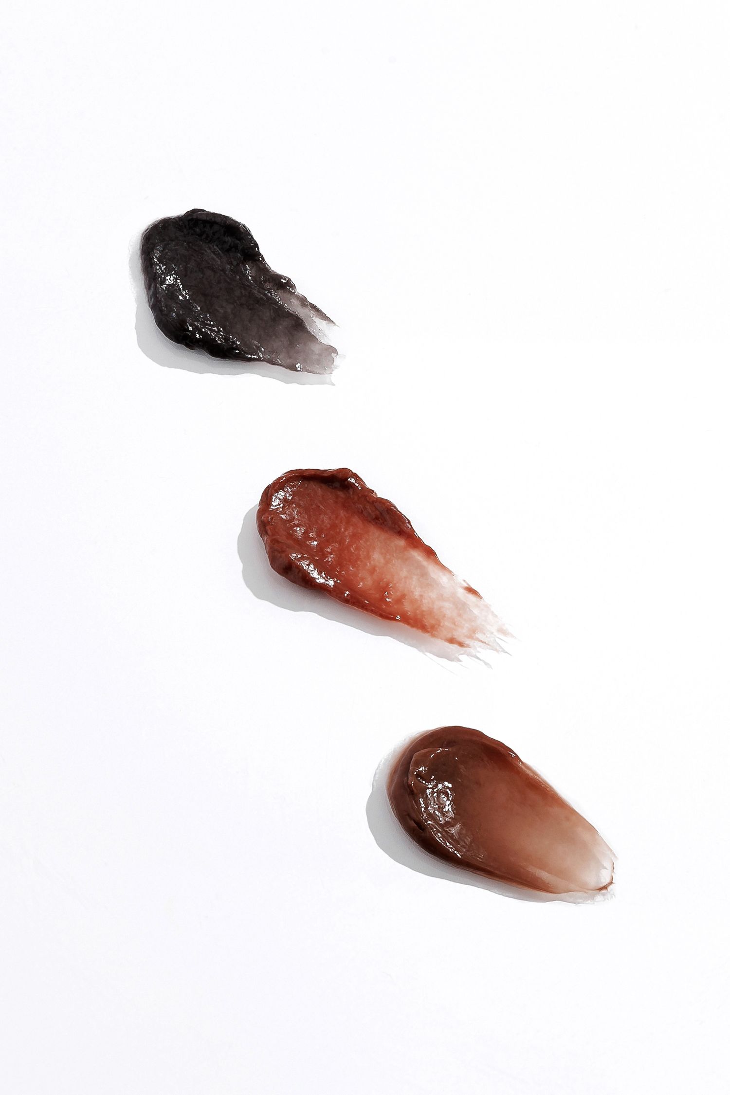 Three swatches of brown and burgundy liquid makeup on white background.