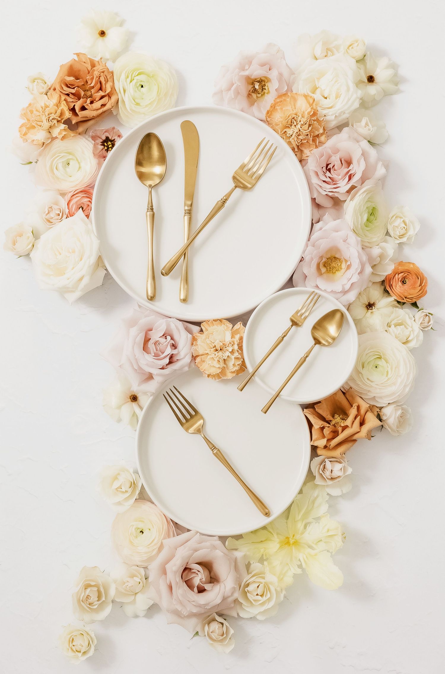 Elegant table setting with gold cutlery and white plates surrounded by pastel roses.