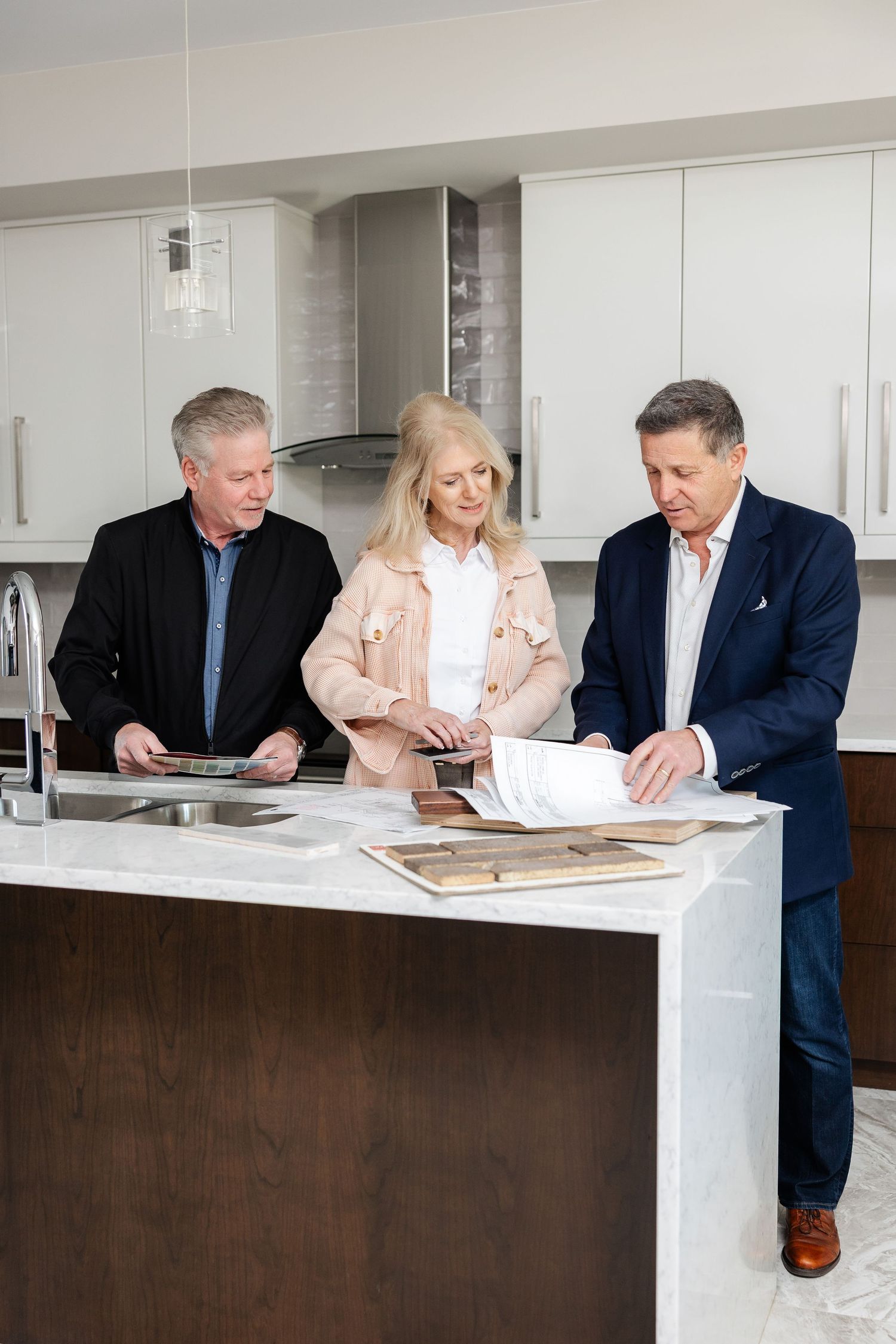 Three professionals reviewing documents and materials at kitchen counter.