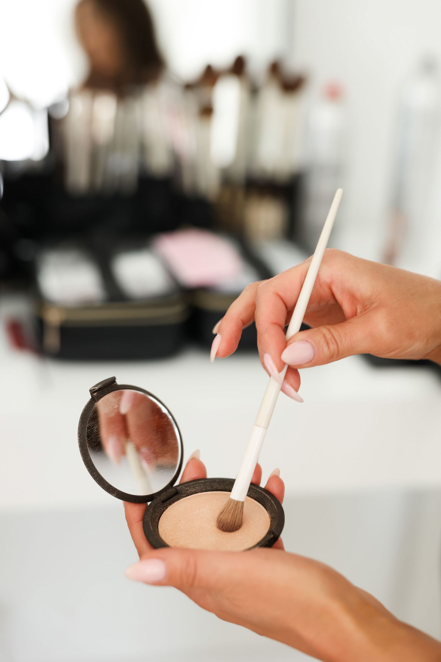 Close-up of hands holding and applying makeup product in bright studio lighting.
