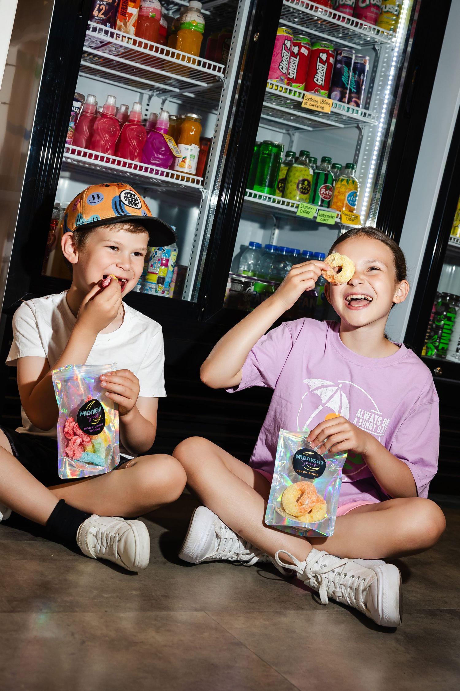 Children sitting on floor enjoying snacks near refrigerated display cases.