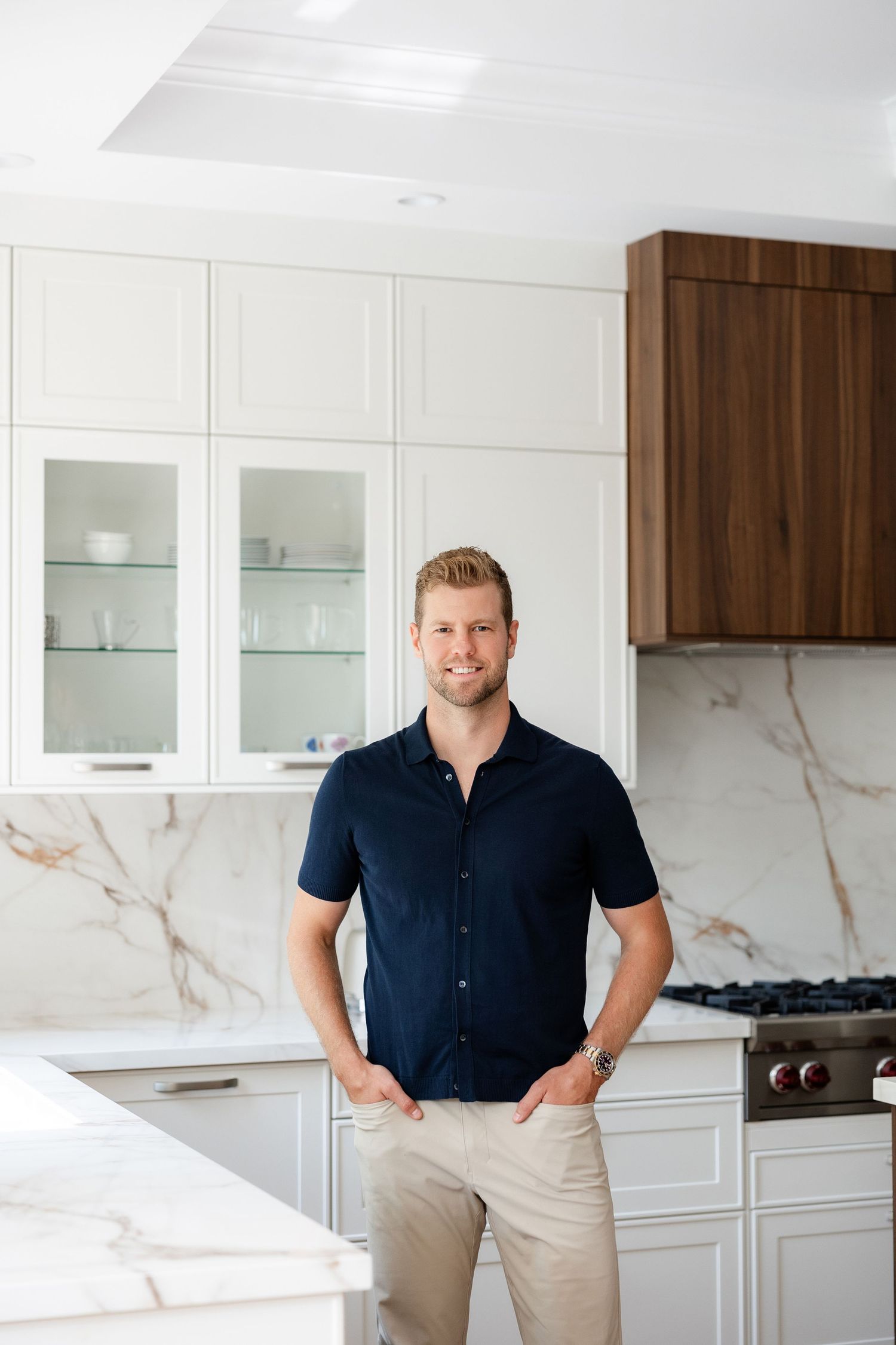 Professional in navy shirt and khakis poses in modern white kitchen.
