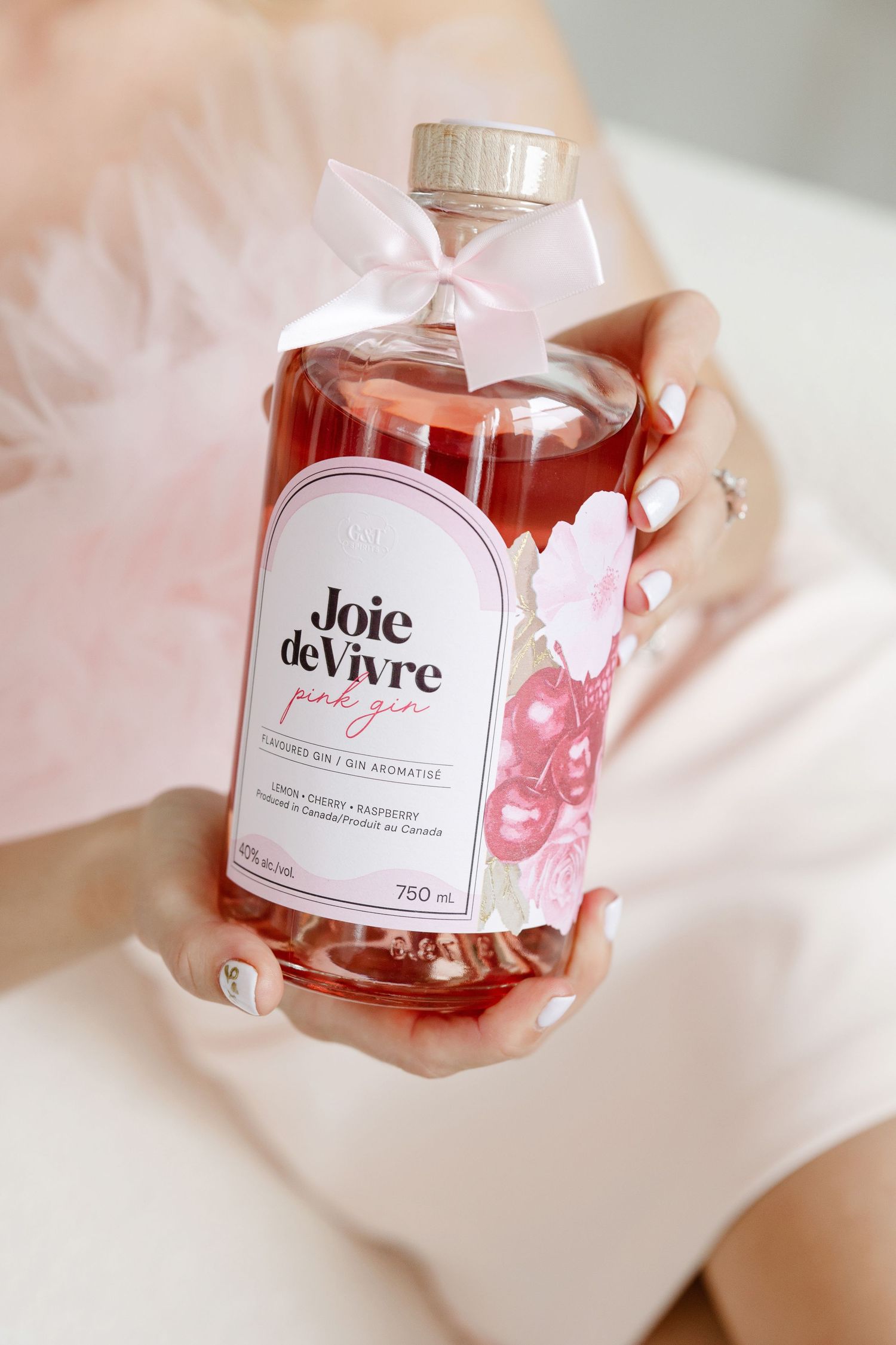 Bottle of Joie de Vivre with pink bow and label held against soft background.