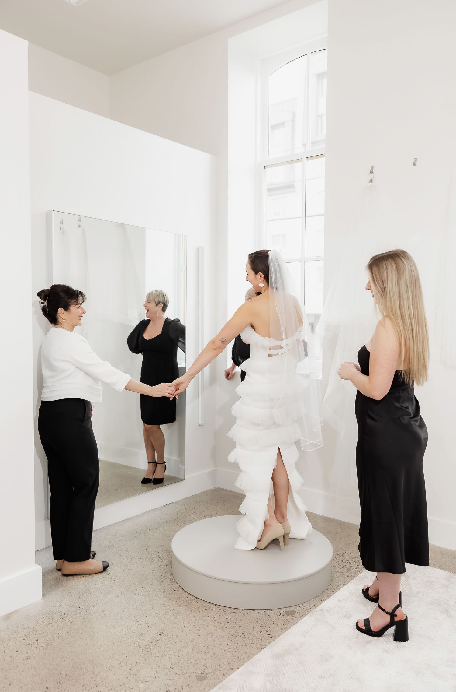 Bridal fitting appointment with multiple stylists helping adjust a wedding gown on a round platform.