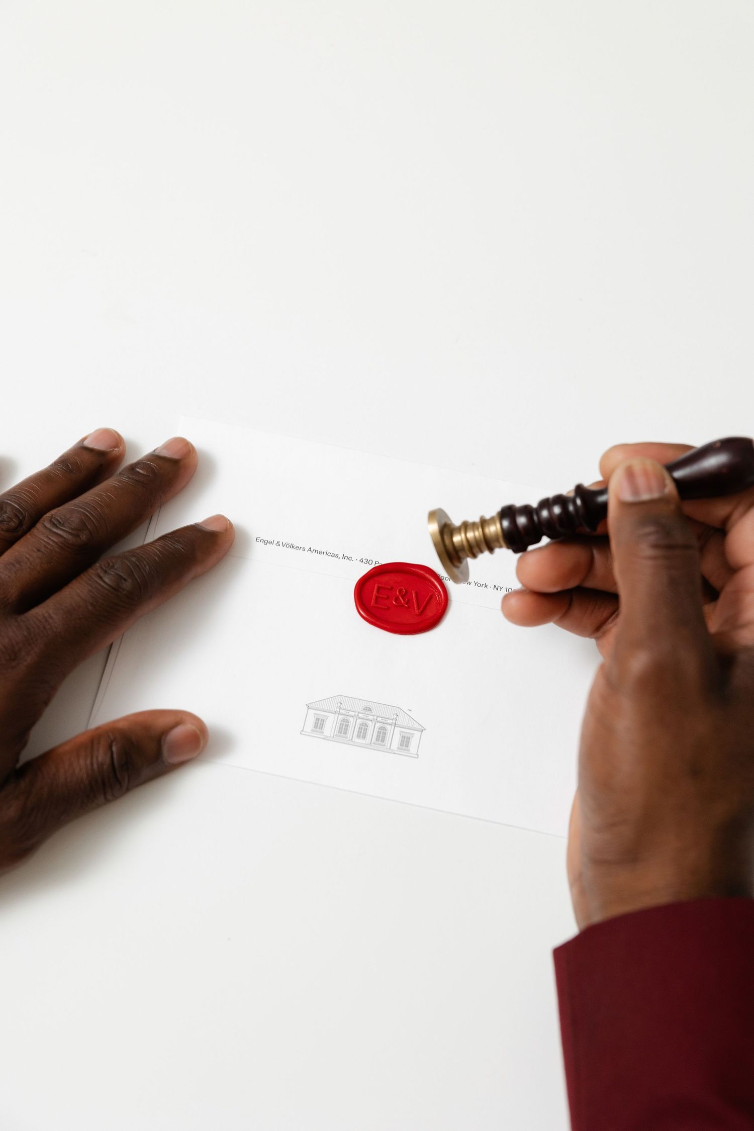 Hand pressing a red wax seal onto a white document with a traditional brass stamp.