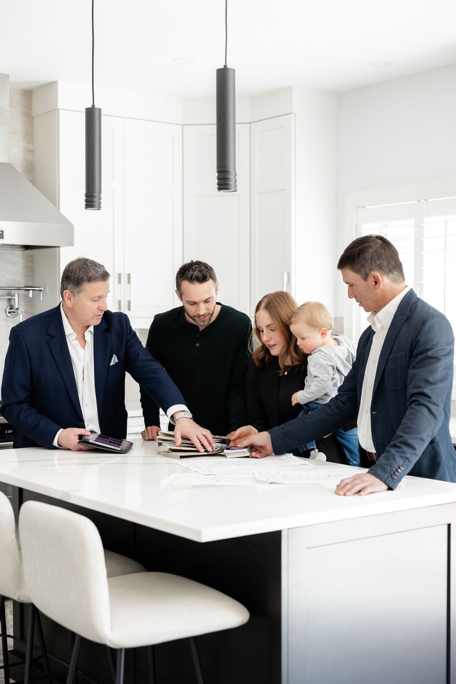 People reviewing documents at sleek white kitchen counter with modern pendant lights.