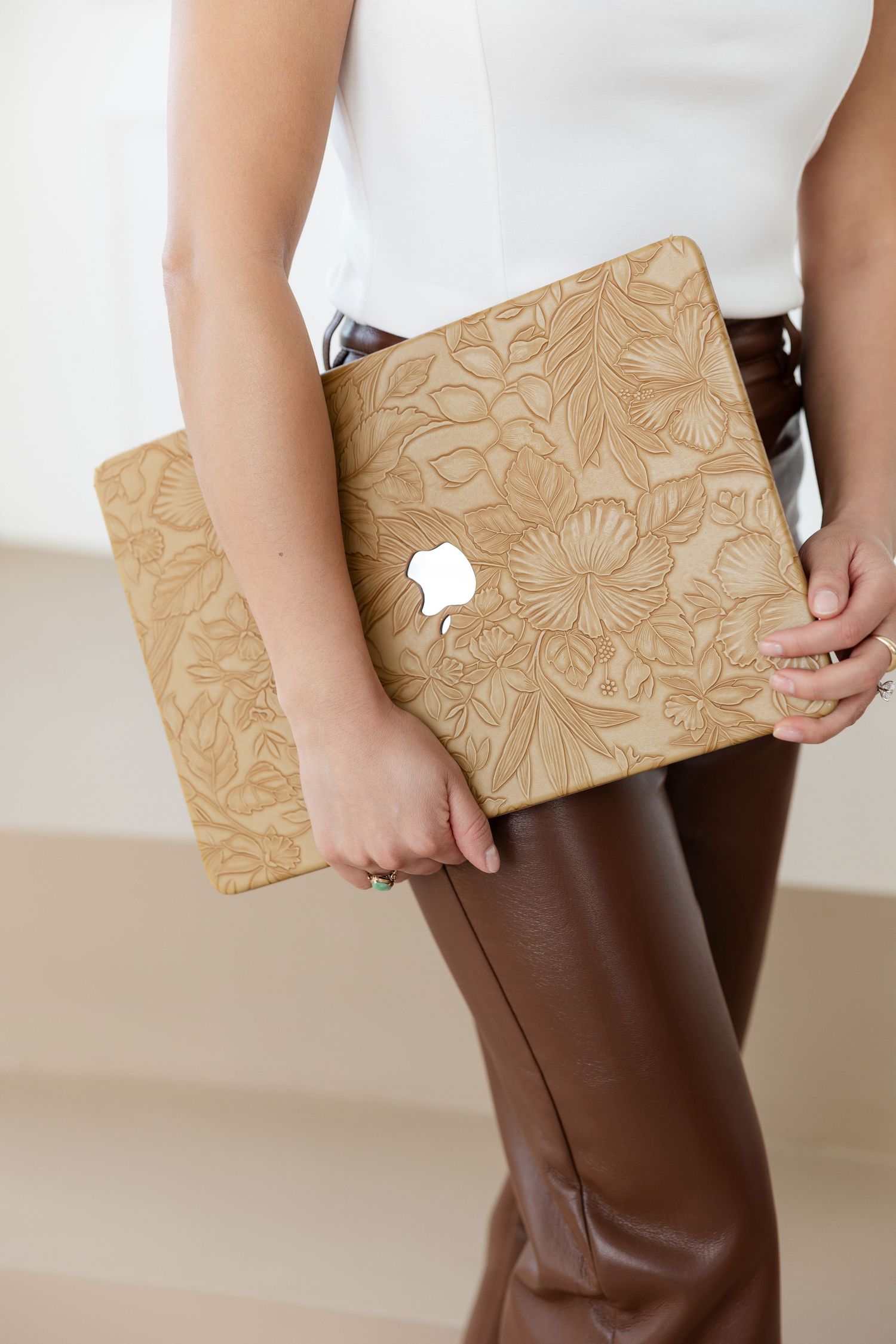 Close-up of floral embossed tan clutch against brown leather pants.